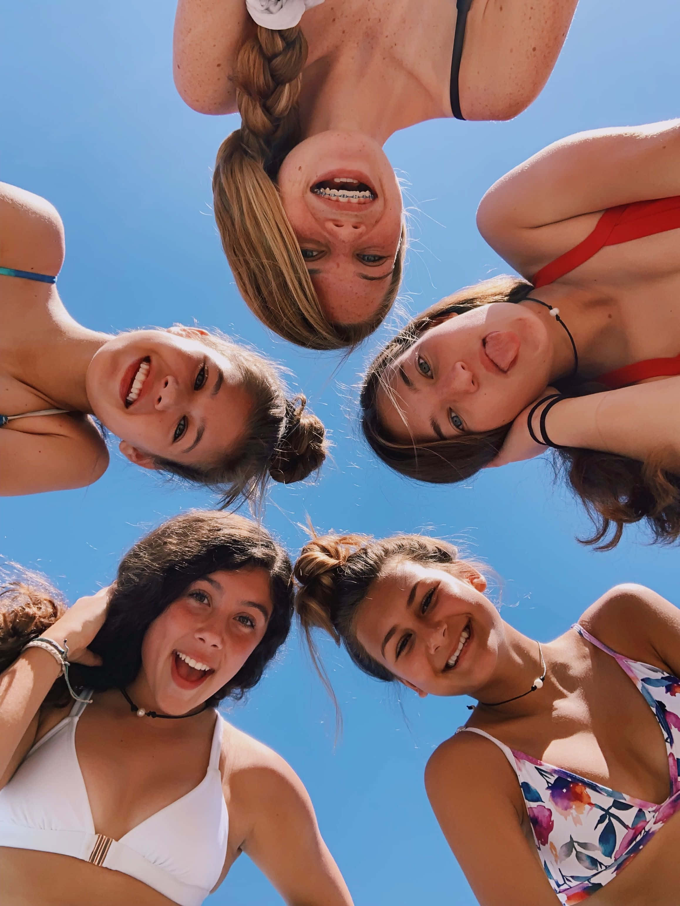 Best Friends 桌布 壁紙 — 五位微笑的年輕女性穿著比基尼圍成一個圓圈，在清澈的藍天下低頭看著相機。