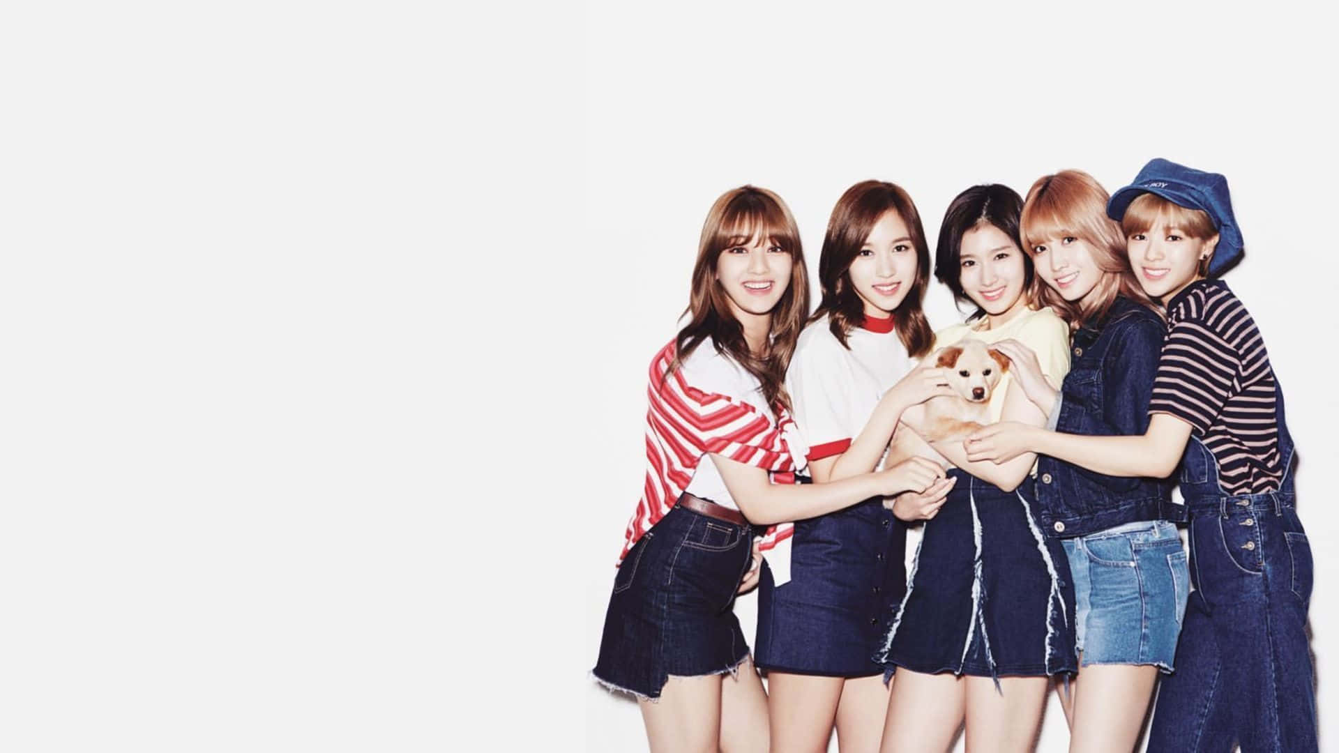 twice 桌布 壁紙 — 五位微笑的年輕女性穿著牛仔服裝，一起抱著一隻小狗，在純白色背景前擺姿勢。