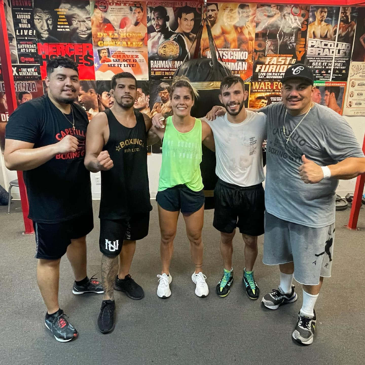 MMA 桌布 壁紙 — 五位微笑的拳擊手穿著健身裝備，在佈滿拳擊海報和沙包的牆前一起擺姿勢。