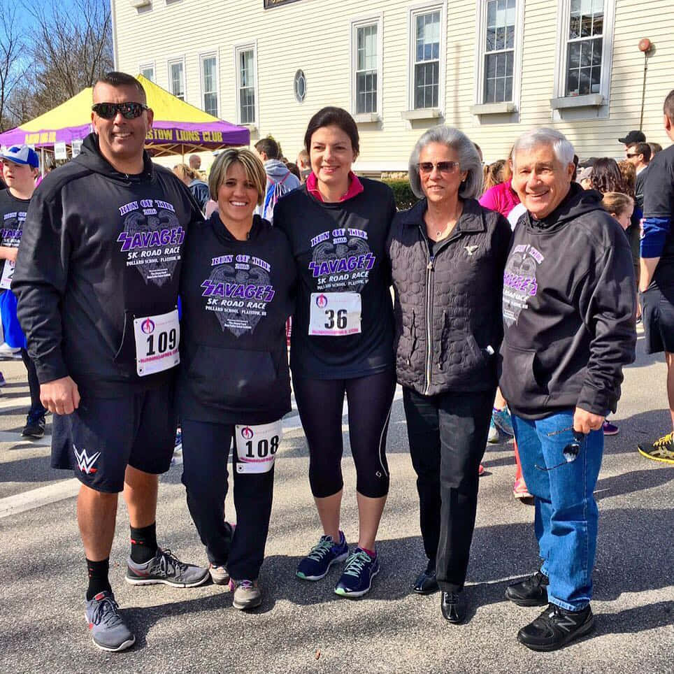 government 桌布 壁紙 — 五位微笑的跑者穿著相配的黑色「Zavagez 5K Road Race」連帽衫，在陽光明媚的戶外起跑線上一同擺姿勢。