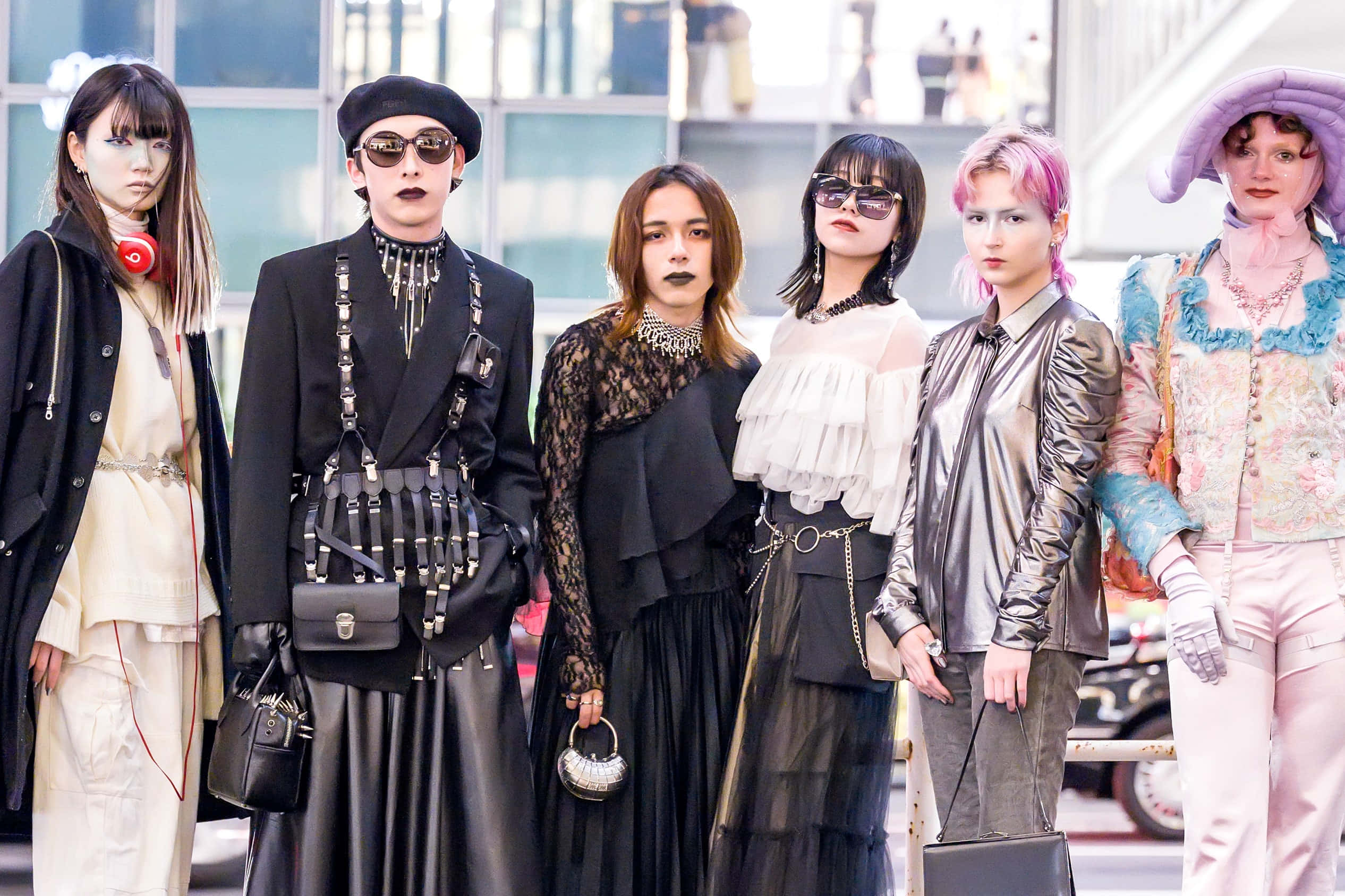 Harajuku Fashion 桌布 壁紙 — 五位時尚前衛的個體穿著前衛服裝，在現代玻璃建築背景下自信地擺姿勢。