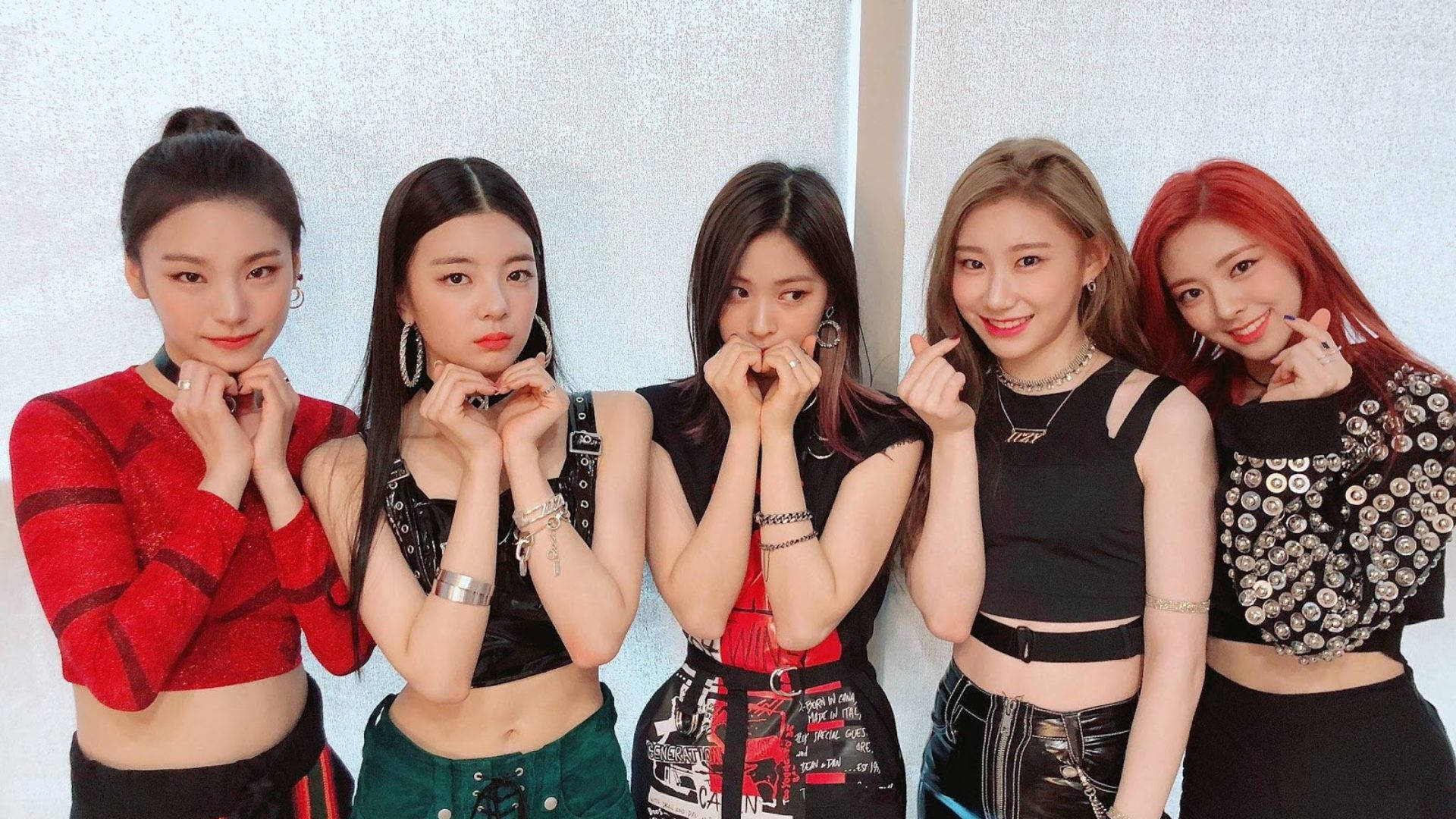 ITZY 桌布 壁紙 — 五位時尚年輕女性穿著潮流服裝，在帶有紋理的白色牆壁前自信地擺出俏皮的手勢。