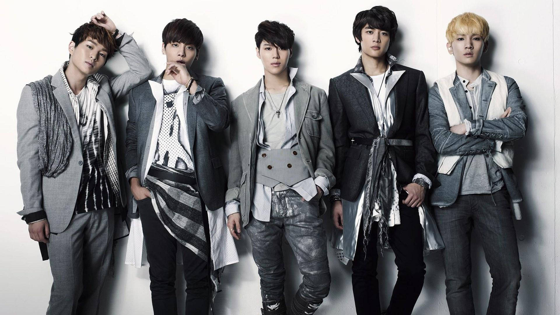 Shinee 桌布 壁紙 — 五位時尚年輕男士穿著潮流分層服裝，在戲劇性燈光下自信地擺姿勢，背景是純白牆壁。