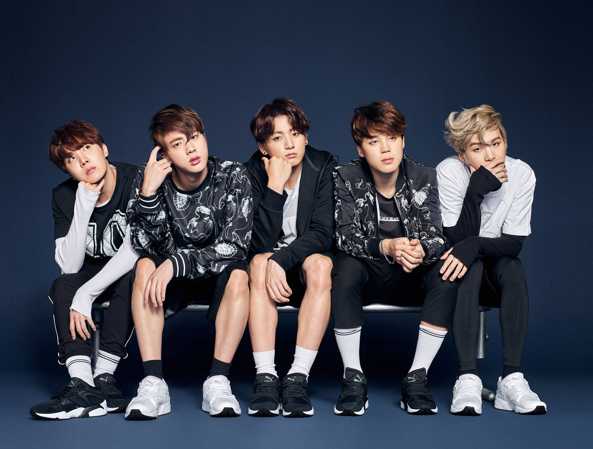 BTS 桌布 壁紙 — 五位時尚年輕男士身穿黑白服裝，在深藍色攝影棚背景前的長椅上自信擺姿勢。
