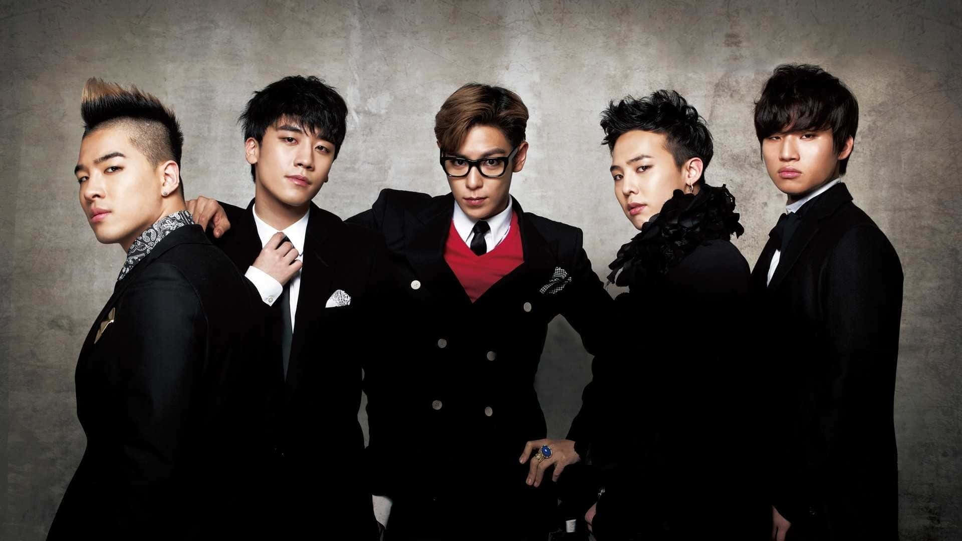 Bigbang 桌布 壁紙 — 五位時尚年輕男士身穿黑色西裝，在帶有紋理的灰色背景前自信地擺姿勢，燈光效果戲劇化。
