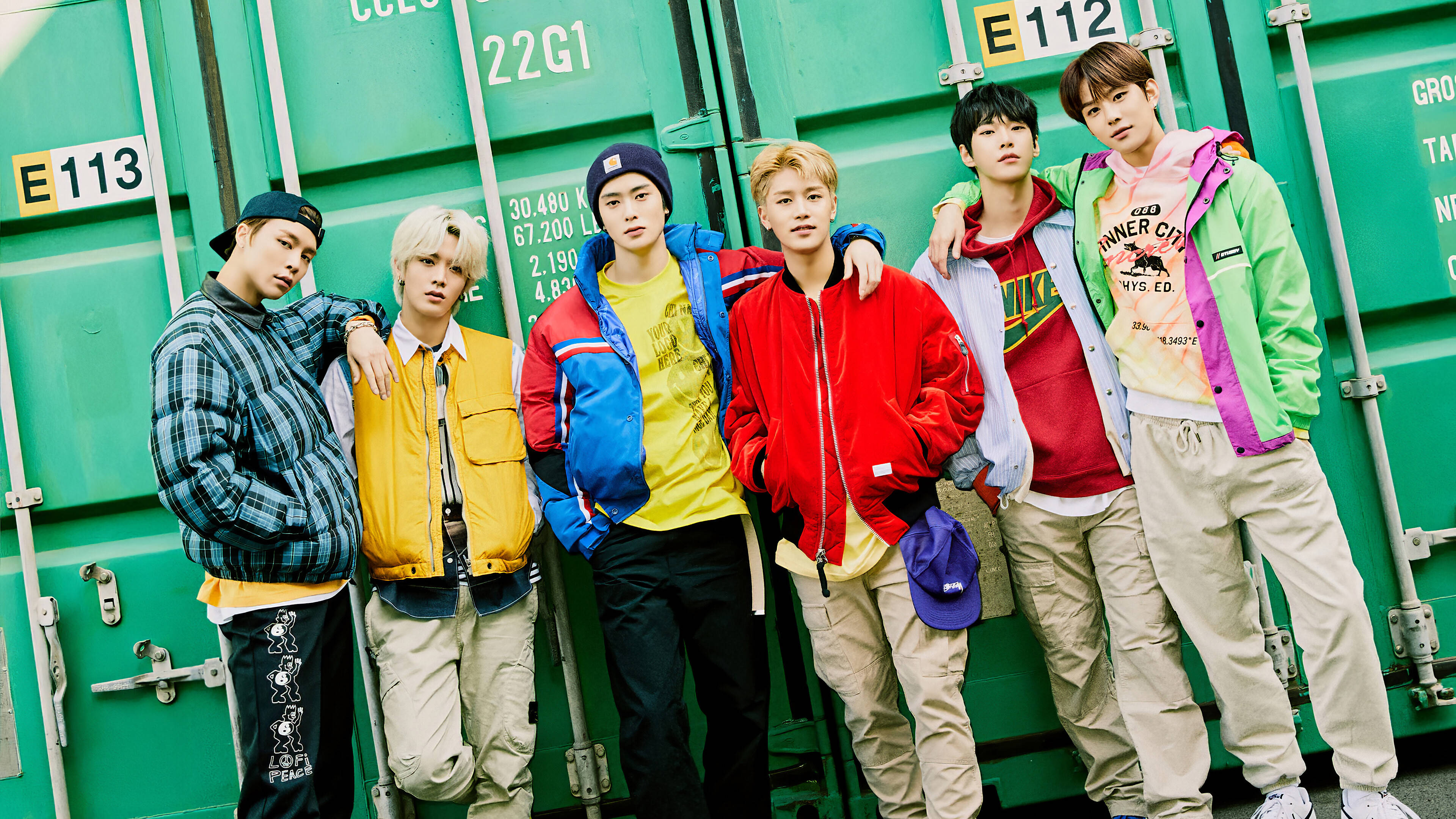 Nct 桌布 壁紙 — 五位時尚年輕男子身穿色彩繽紛的街頭服飾，在充滿活力的綠色貨櫃背景前自信地擺姿勢。