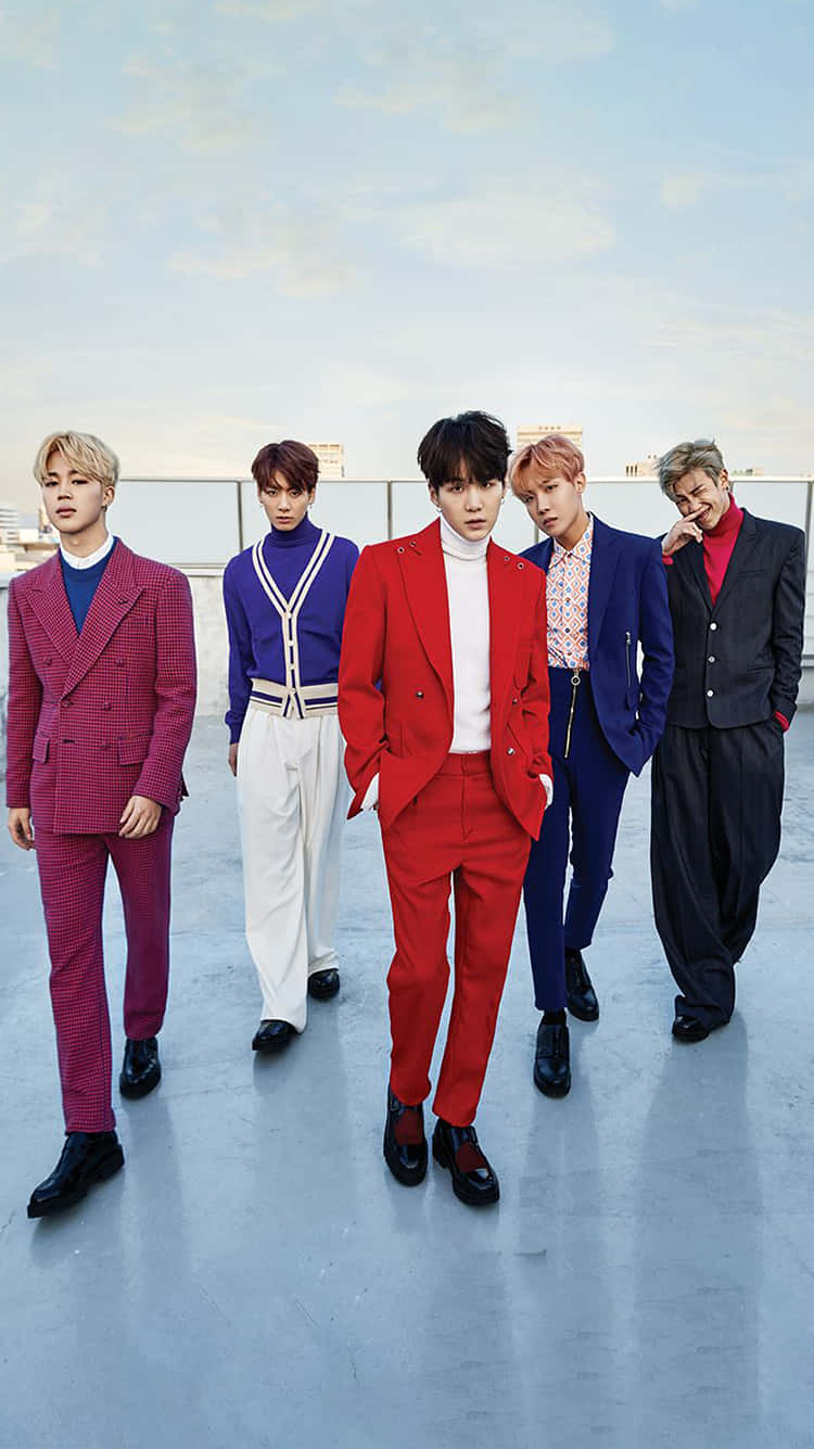 BTS 桌布 壁紙 — 五位時尚男士穿著大膽色彩的西裝，在柔和藍天下自信地在屋頂上擺姿勢。