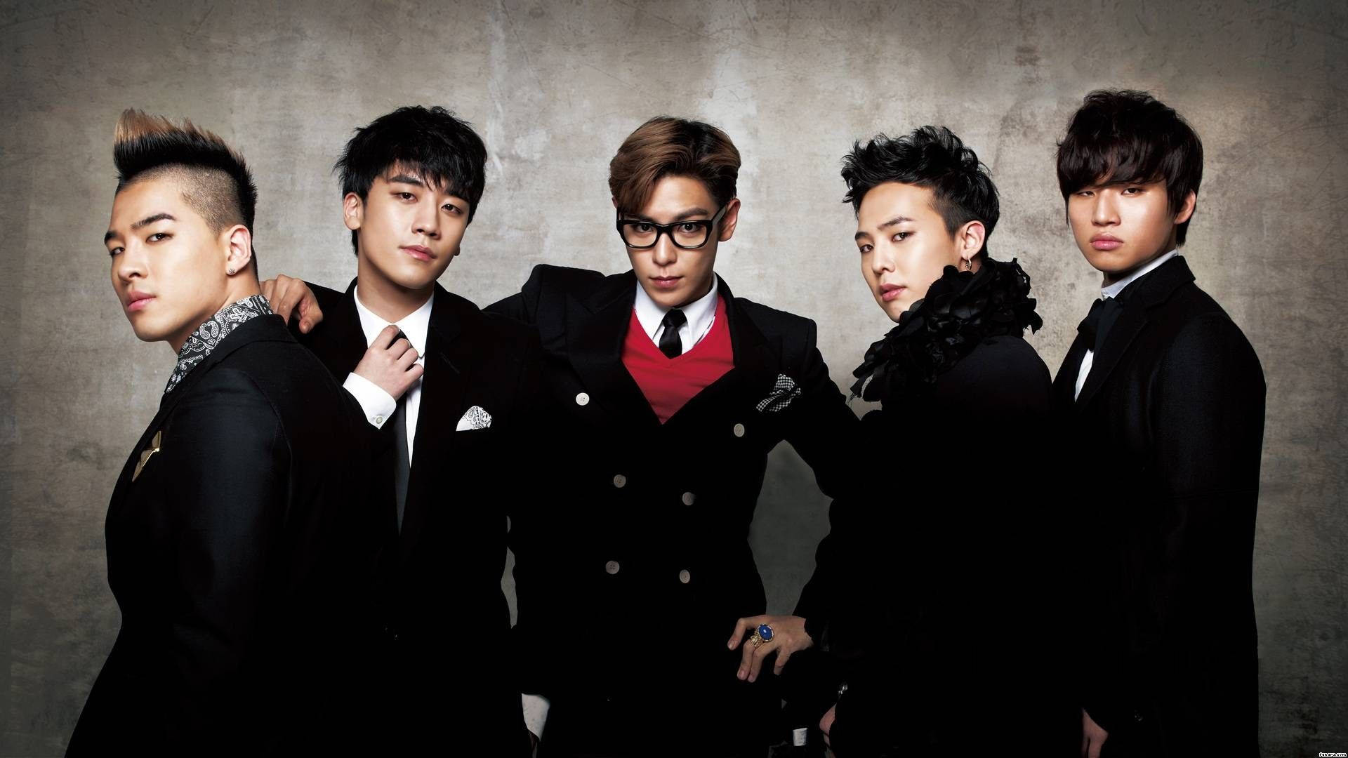 Bigbang 桌布 壁紙 — 五位時尚男士身穿黑色西裝，在紋理灰色牆壁前自信地擺姿勢，燈光效果戲劇化。