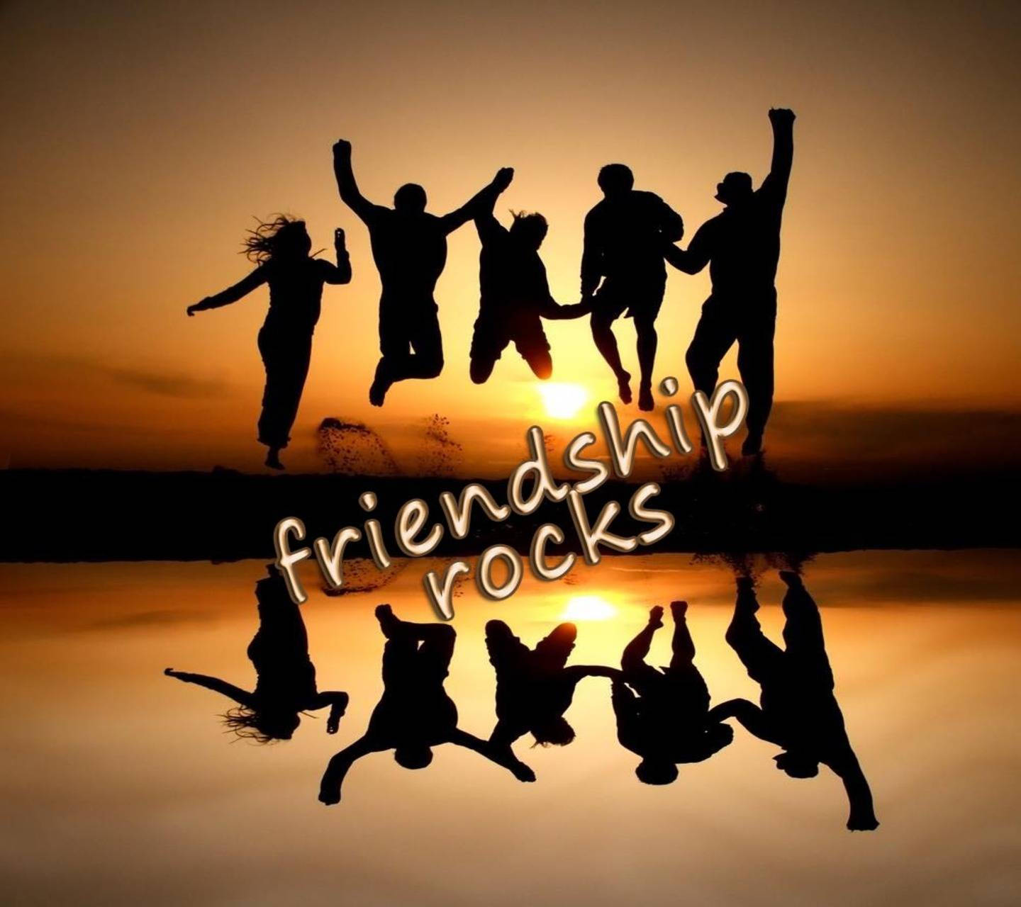 group 桌布 壁紙 — 五位朋友在日落時快樂地跳躍，他們的剪影倒映在水中，下方有發光的「friendship rocks」文字。