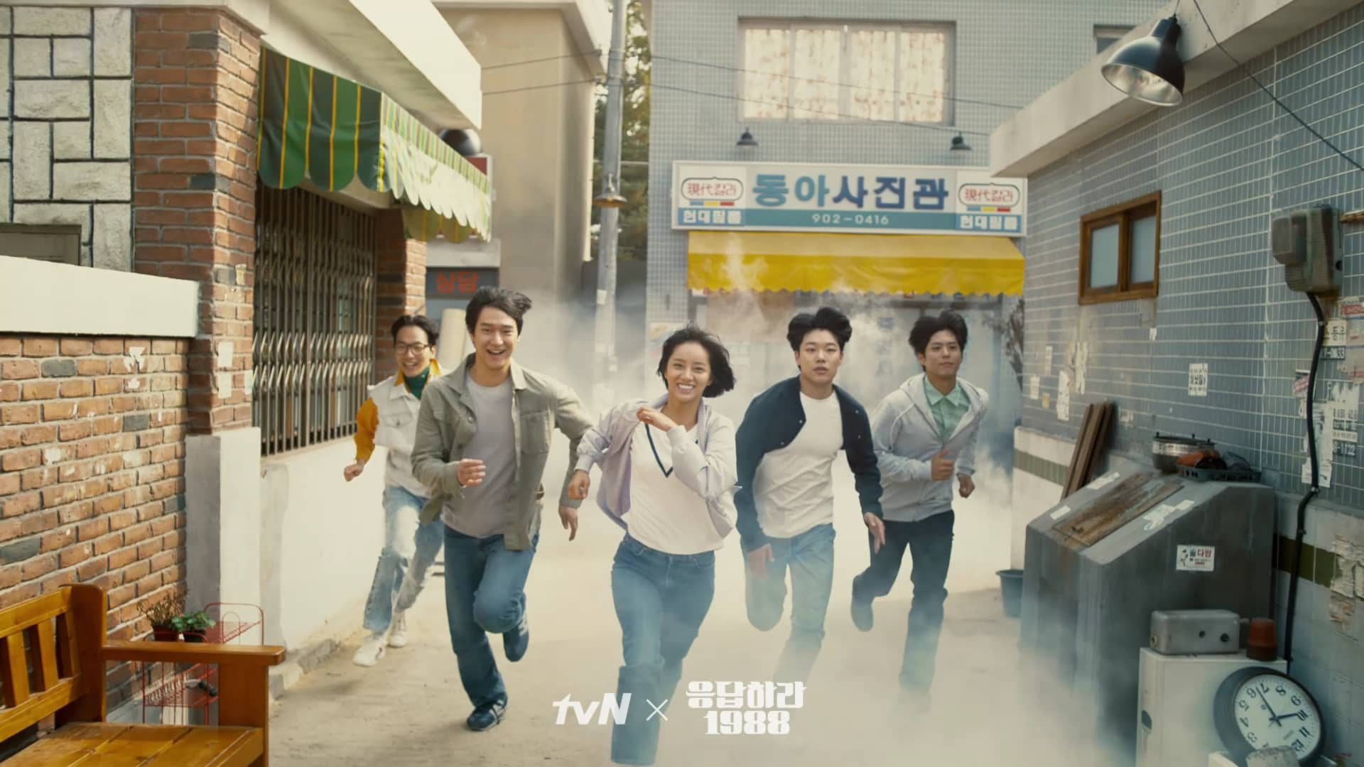 Reply 1988 桌布 壁紙 — 五位朋友愉快地跑下一條煙霧瀰漫的韓國小巷，經過磚砌建築和復古店面。