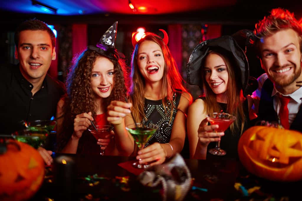 Party 桌布 壁紙 — 五位朋友穿著萬聖節服裝，在色彩繽紛的俱樂部燈光下笑著用雞尾酒乾杯。