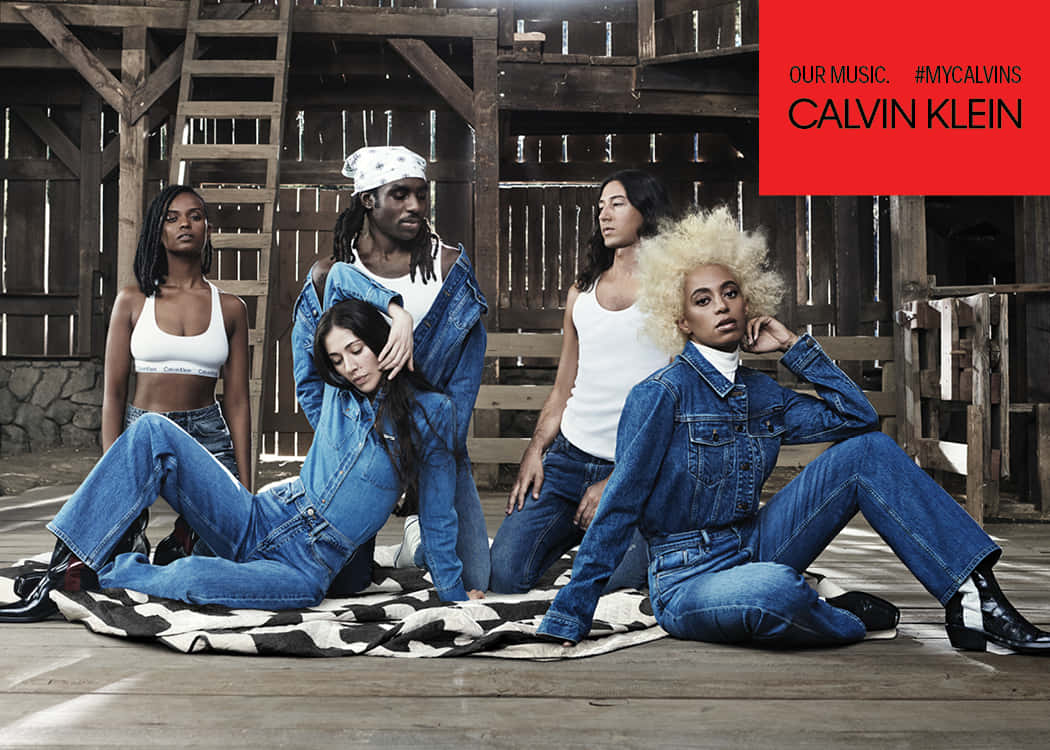 Calvin Klein 桌布 壁紙 — 五位模特兒穿著牛仔服裝，在質樸的木穀倉內的花紋毯子上自信地擺姿勢。