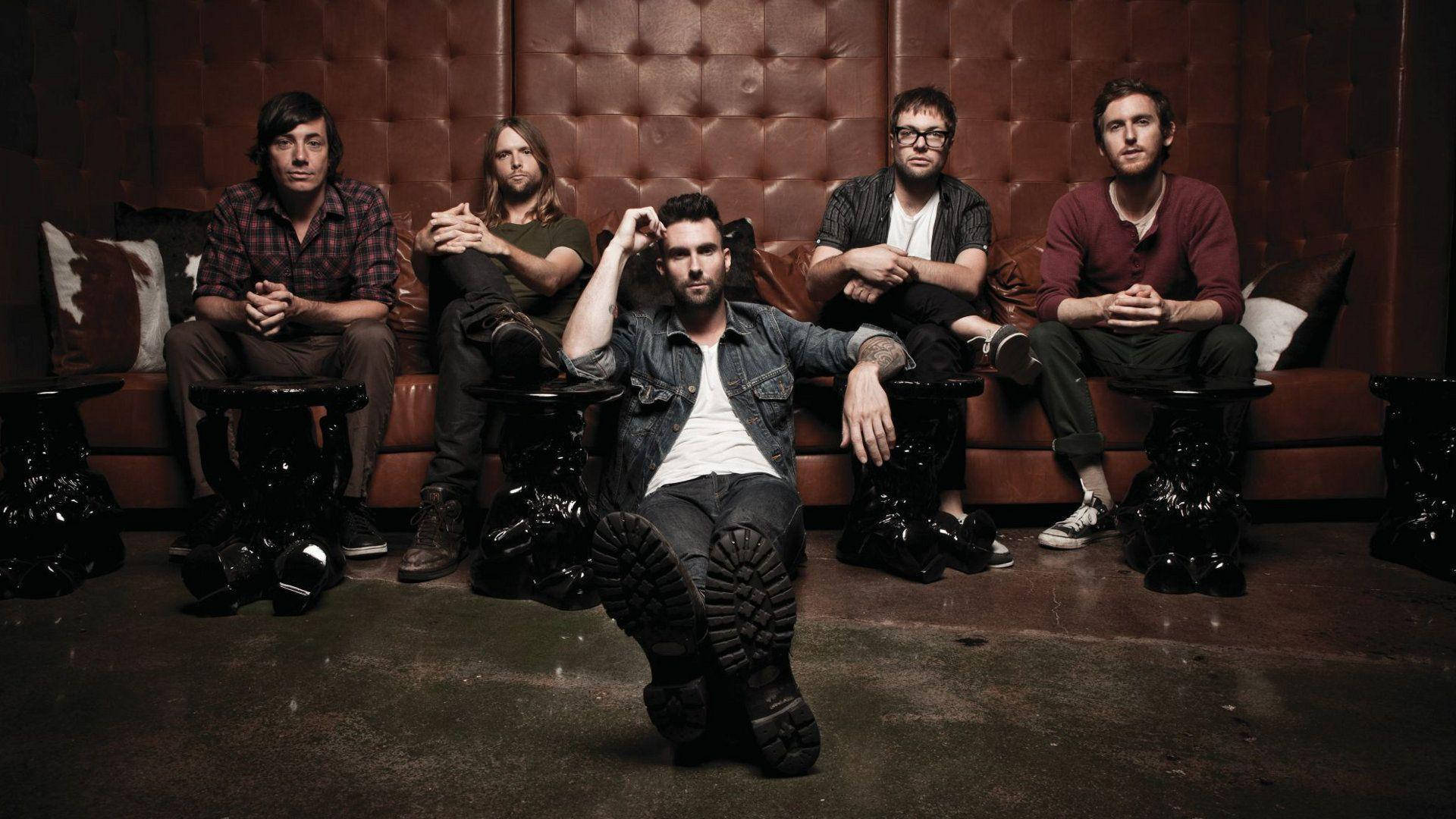 maroon 5 桌布 壁紙 — 五位男士穿著休閒服裝，在光線昏暗的休息室裡，自信地坐在簇絨皮革沙發上，地板深色，旁邊有華麗的邊桌。
