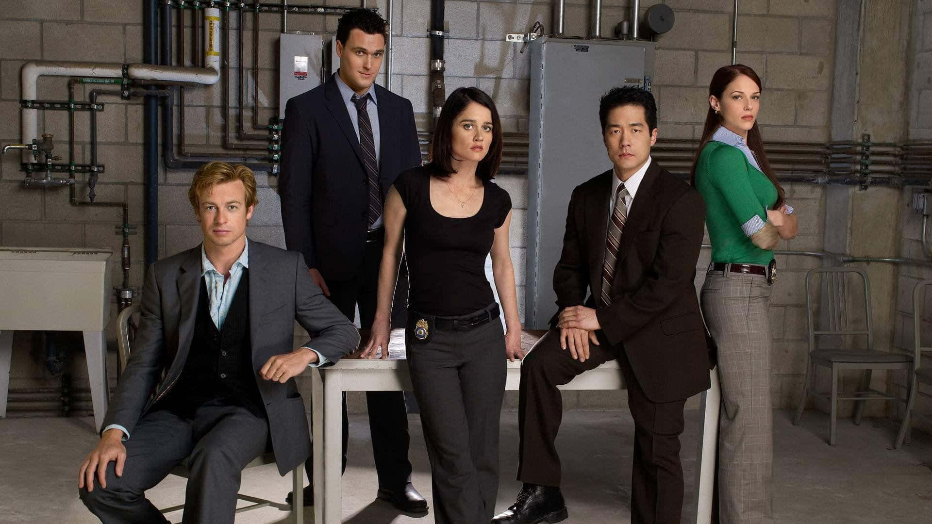 Robin Tunney 桌布 壁紙 — 五位穿著正式服裝的演員在一個佈滿外露管道和混凝土牆壁的粗糙工業房間中自信地擺姿勢。