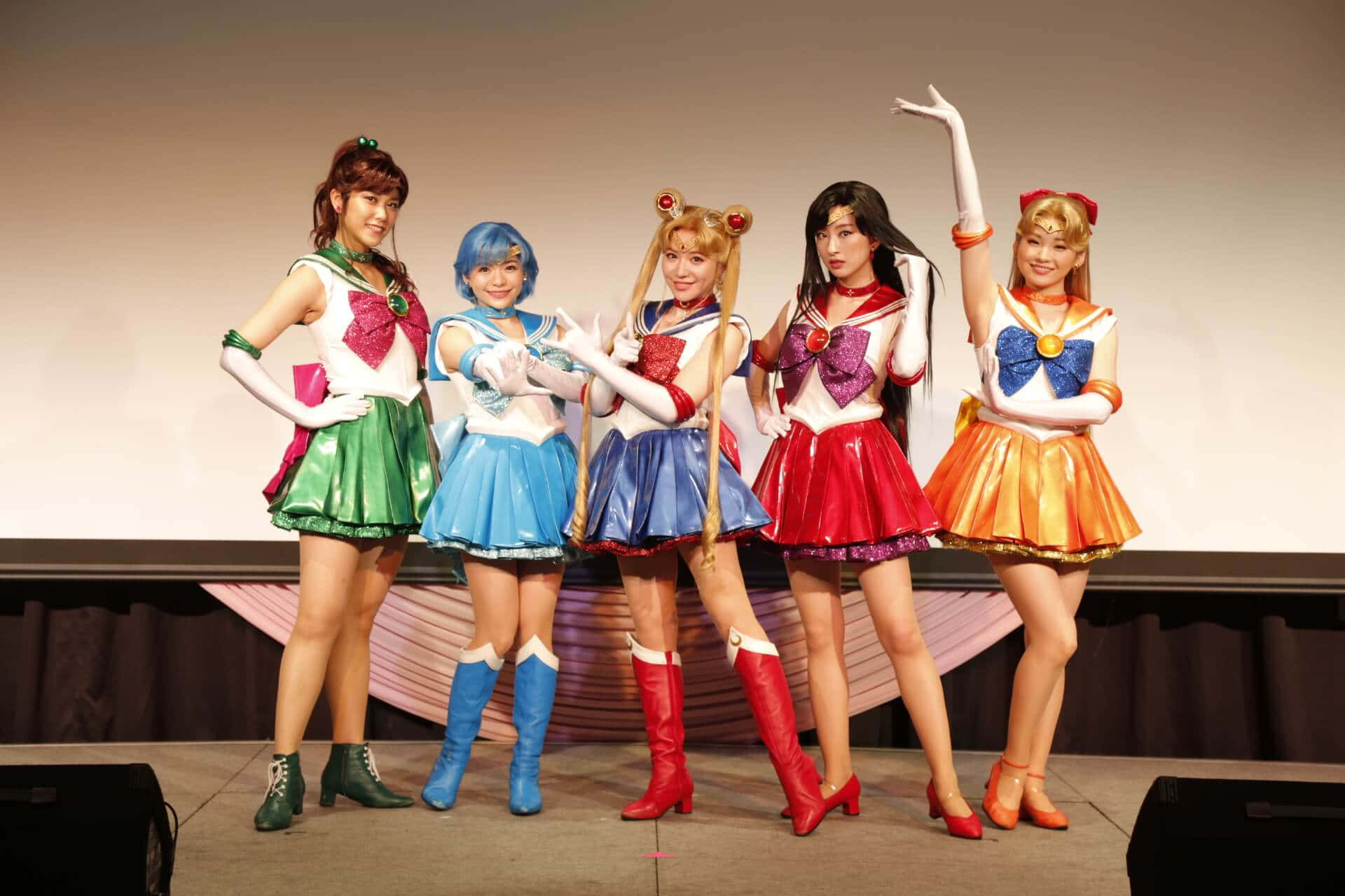 Tokyo Japan 桌布 壁紙 — 五位穿著美少女戰士服裝的cosplayer在舞台上自信地擺姿勢，穿著色彩繽紛的裙子和靴子。