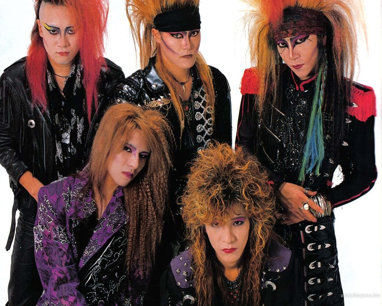 Visual Kei 桌布 壁紙 — 五位華麗金屬樂團成員，頭髮蓬鬆、妝容大膽、身穿皮革服裝，在純白背景前擺姿勢。