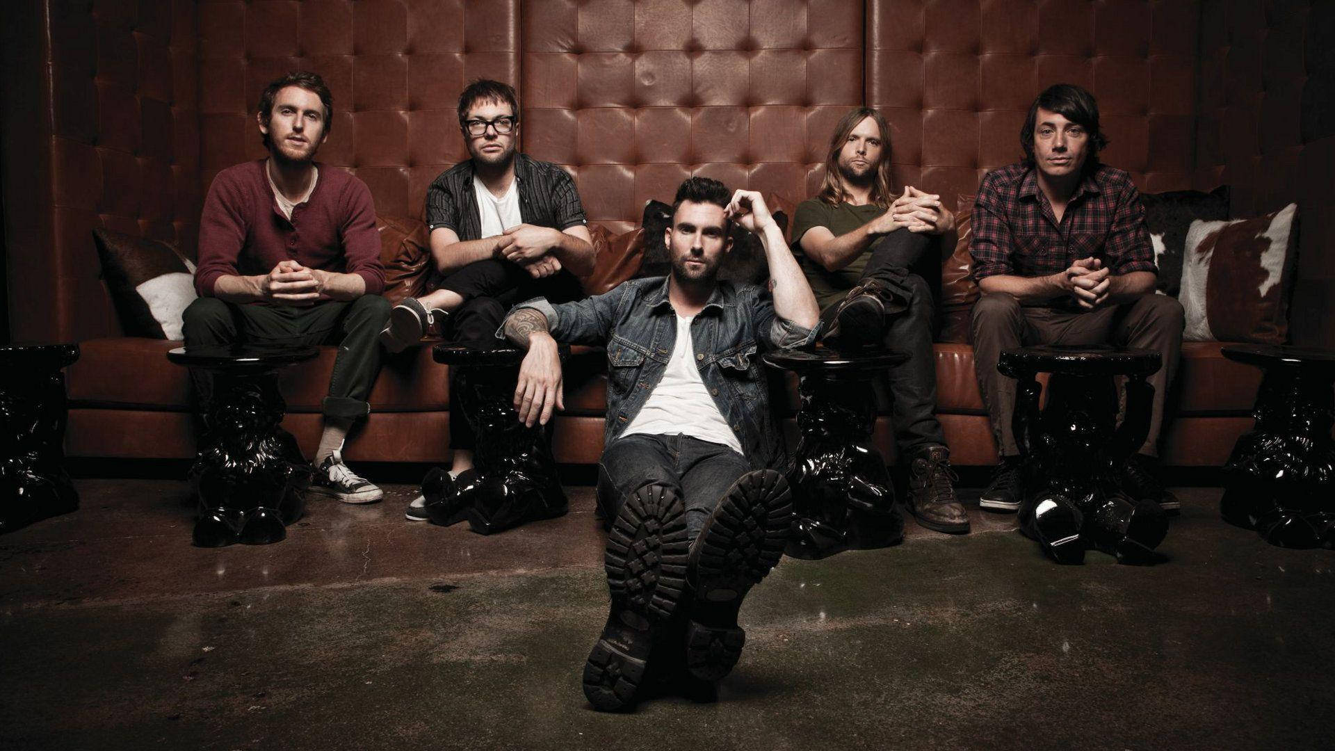 maroon 5 桌布 壁紙 — 五位身穿休閒服裝的男士自信地坐在一張簇絨皮革沙發上，身處燈光昏暗、氣氛憂鬱的休息室，地板深色，並有華麗的邊桌。