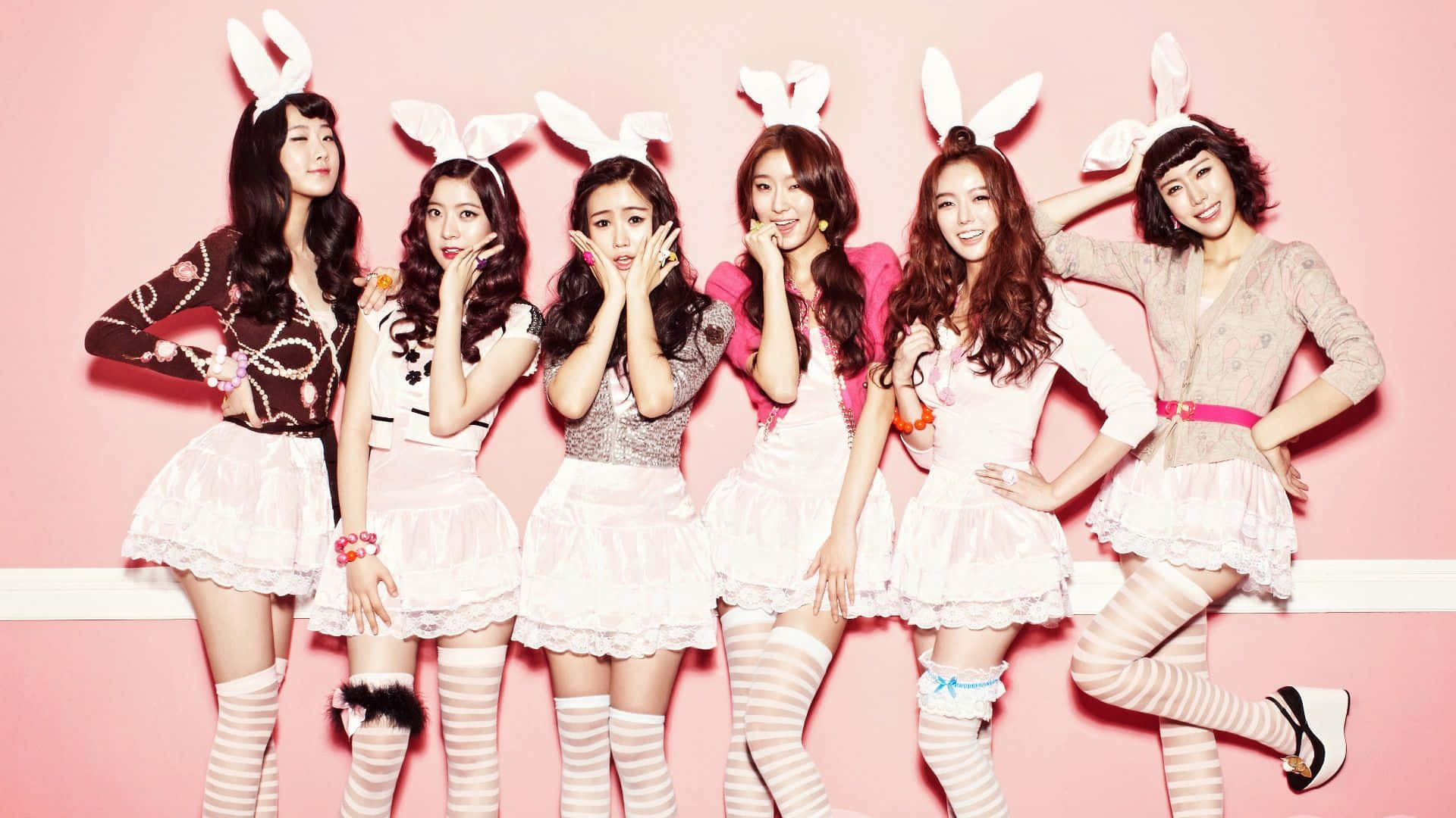 K-pop 桌布 壁紙 — 五位身穿兔女郎服裝的女性，在粉紅色的牆前擺出俏皮的姿勢，穿著條紋長襪和荷葉邊短裙。