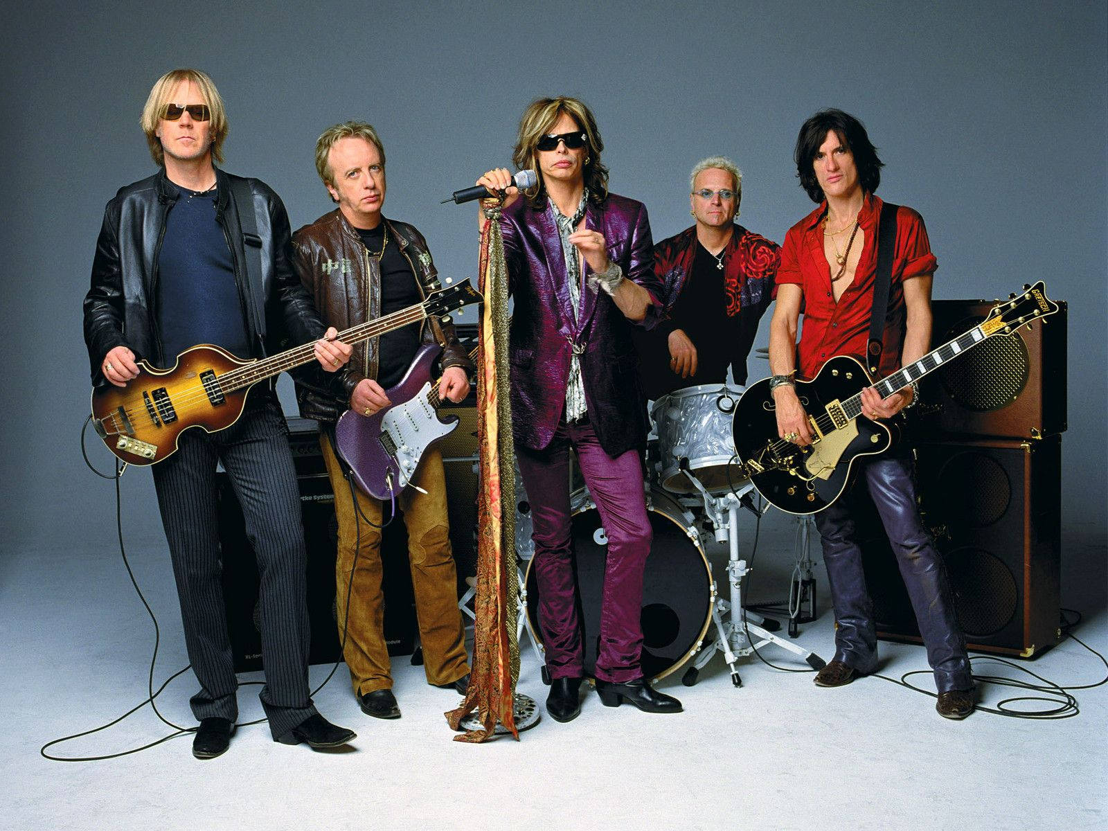 Aerosmith 桌布 壁紙 — 五位身穿皮革和紫色天鵝絨的搖滾音樂家，在純灰色攝影棚背景前，手持吉他和鼓擺姿勢。