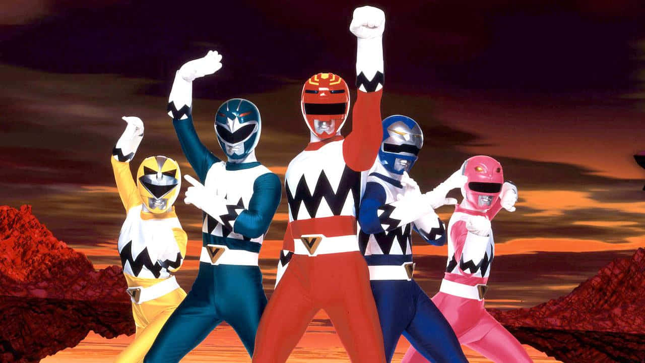 金剛戰士 桌布 壁紙 — 五位身穿色彩繽紛戰衣的Power Rangers在紅色岩石地形上，以英雄姿態對抗熾熱的夕陽。