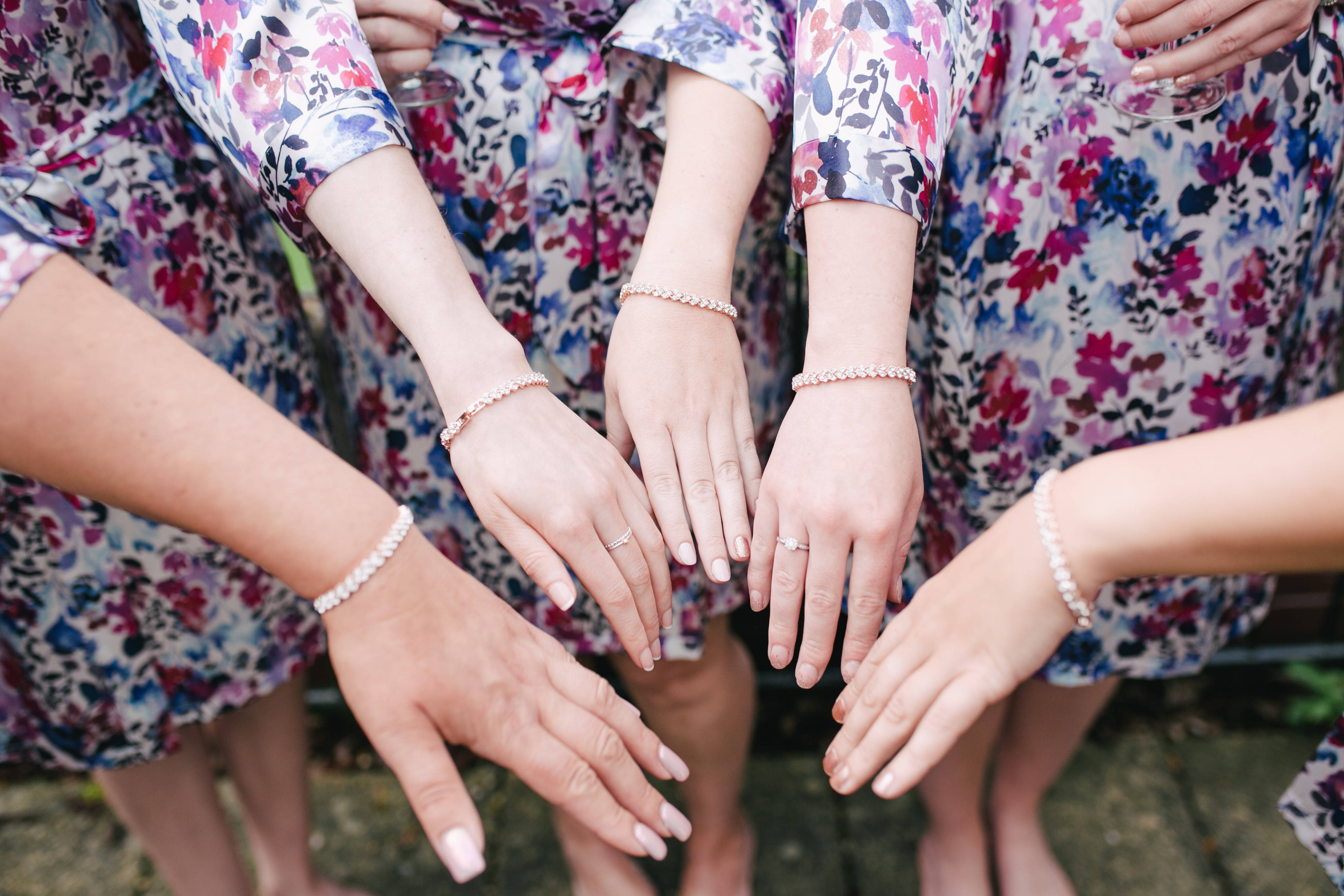 Bridesmaids 桌布 壁紙 — 五位身穿花卉連衣裙的女性近距離特寫，戴著珍珠手鐲和戒指，手牽手進行歡樂的慶祝。