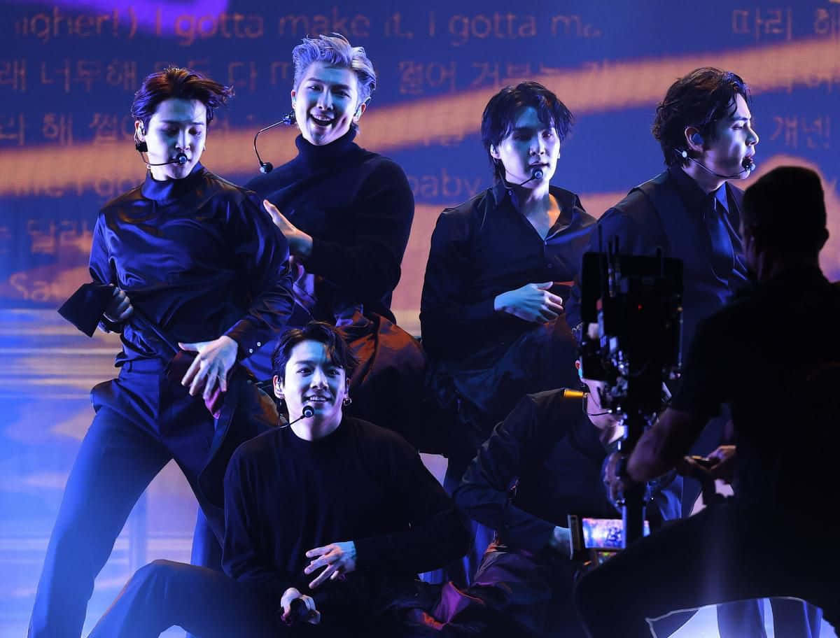 K-pop 表演者在藍色燈光下於舞台上跳舞，背後投射著歌詞。 — 防彈少年團 合照 壁紙