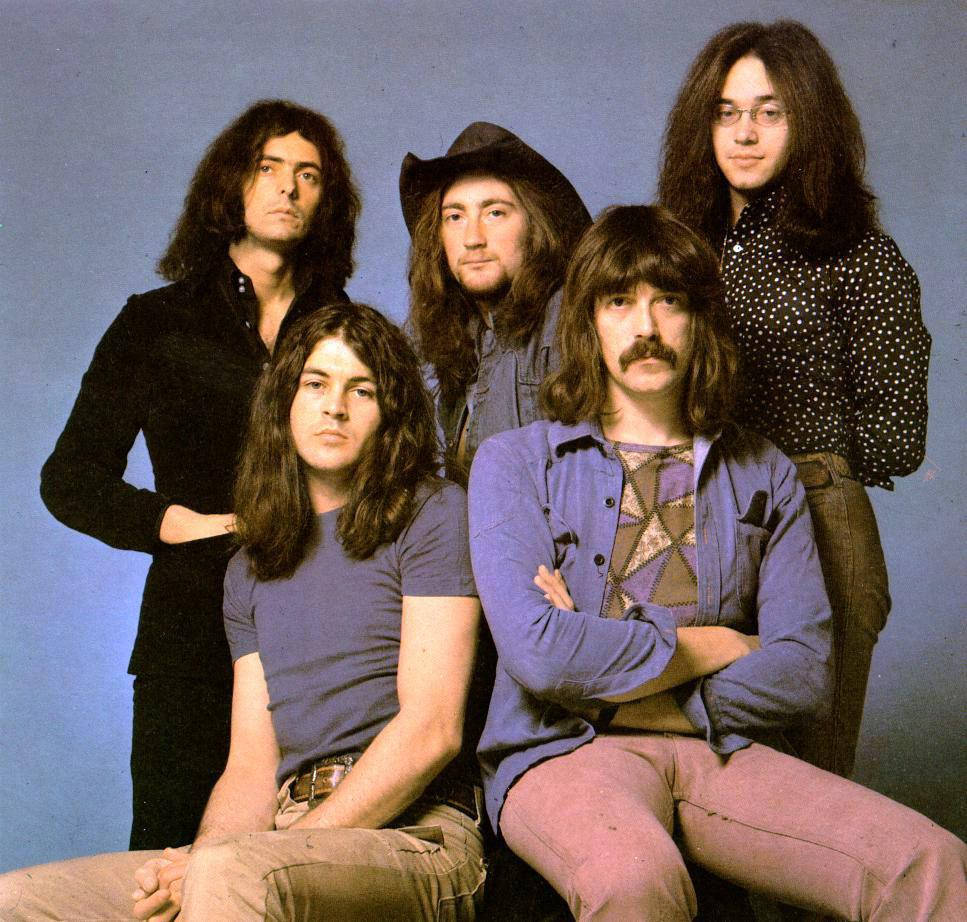 deep purple 桌布 壁紙 — 五位長髮男士身穿1970年代搖滾服裝，在純藍色攝影棚背景前自信地擺姿勢。