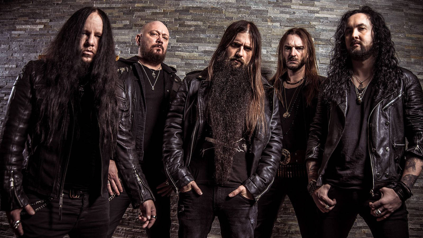 Joey Jordison 桌布 壁紙 — 五位長髮鬍鬚的重金屬樂隊成員穿著黑色皮夾克，在石牆前擺出強烈的姿勢。