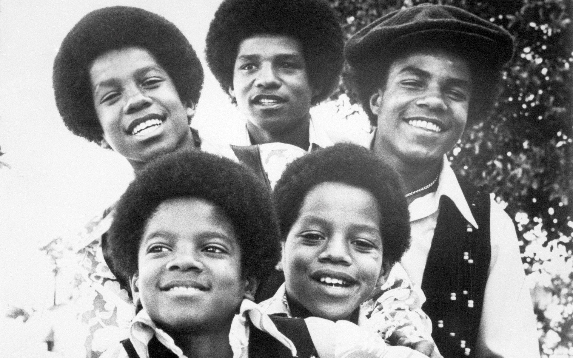 Jackson 5 桌布 壁紙 — 五位面帶微笑、留著非洲式髮型、穿著時尚70年代服裝的年輕男性，在經典黑白照片中一起在戶外擺姿勢。
