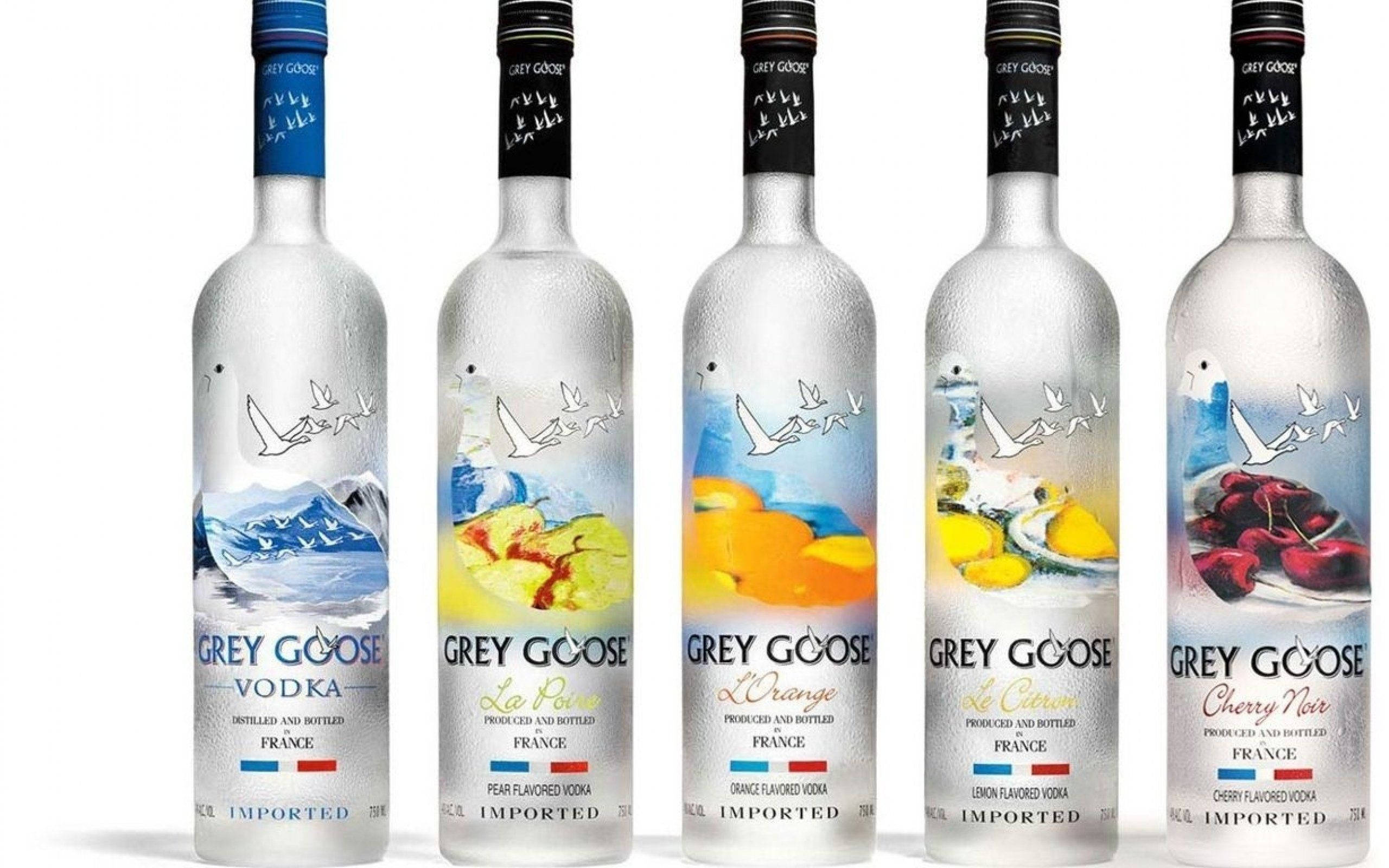 Drink 桌布 壁紙 — 五個Grey Goose伏特加酒瓶，帶有獨特的口味標籤和結霜的玻璃表面，置於潔淨的白色背景前。