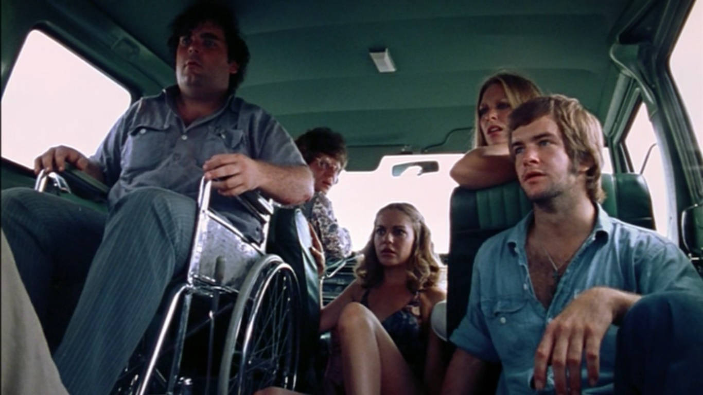Texas Chainsaw Massacre 桌布 壁紙 — 五個人，包括一名坐輪椅的男子，坐在一輛復古車內，表情嚴肅地向前看。