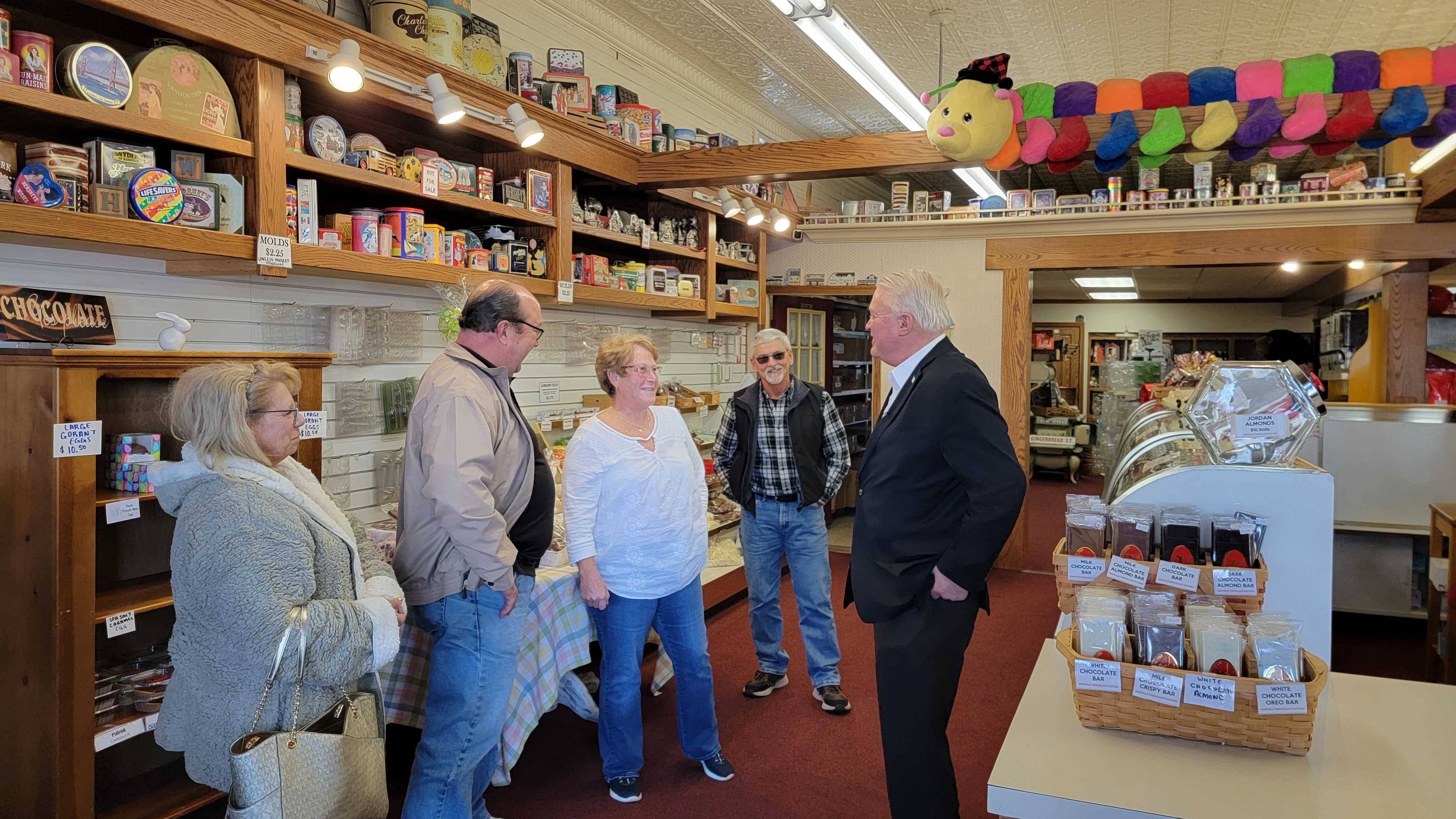 Politics 桌布 壁紙 — 五個人在一間舒適、貨品齊全的專門食品店裡熱情聊天，店內有木架和色彩繽紛的掛飾。