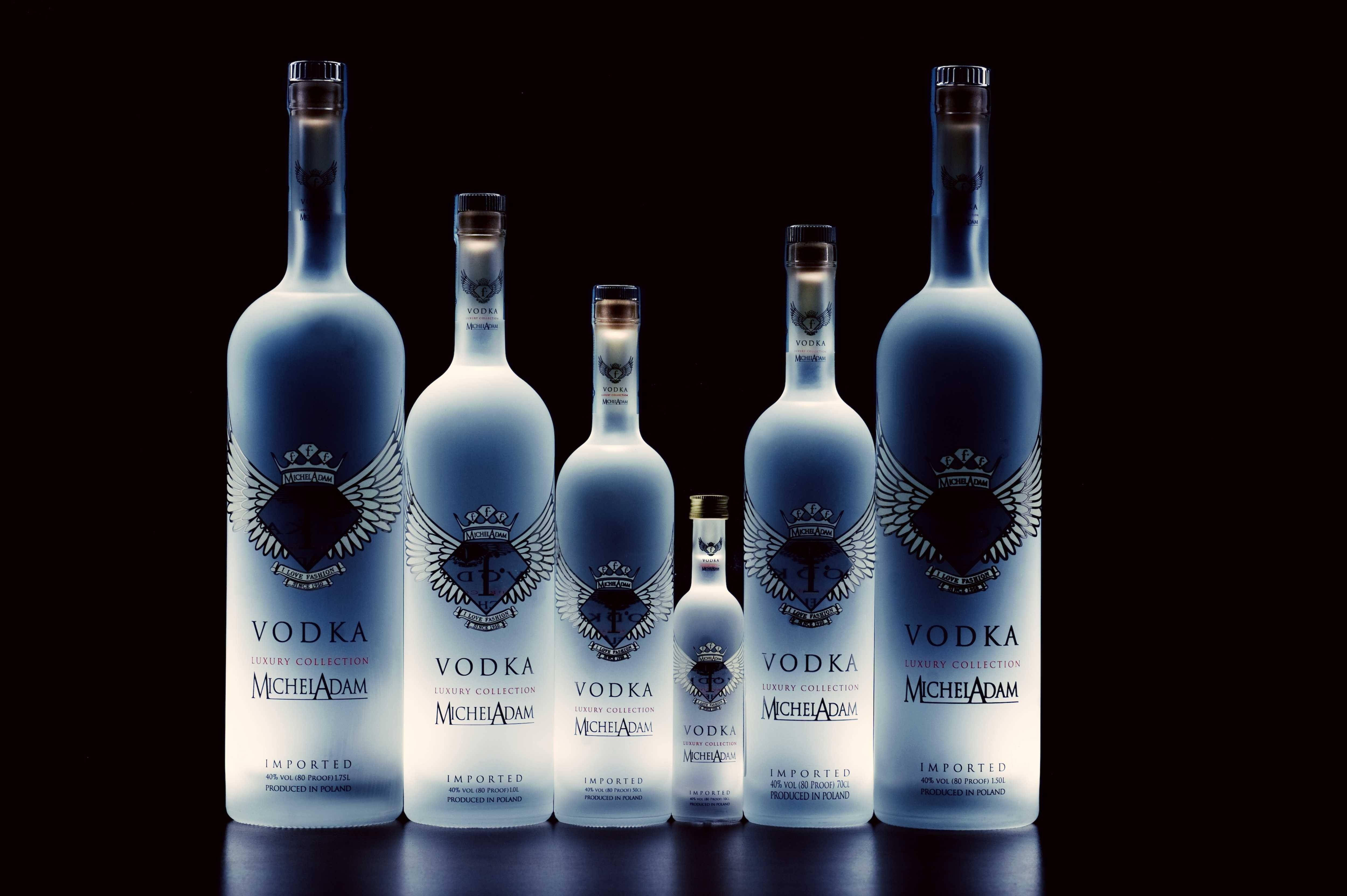 alcohol 桌布 壁紙 — 五個優雅的藍色 Michel Adam 伏特加酒瓶，按大小遞減排列在反光的黑色表面上，搭配戲劇性的工作室燈光。