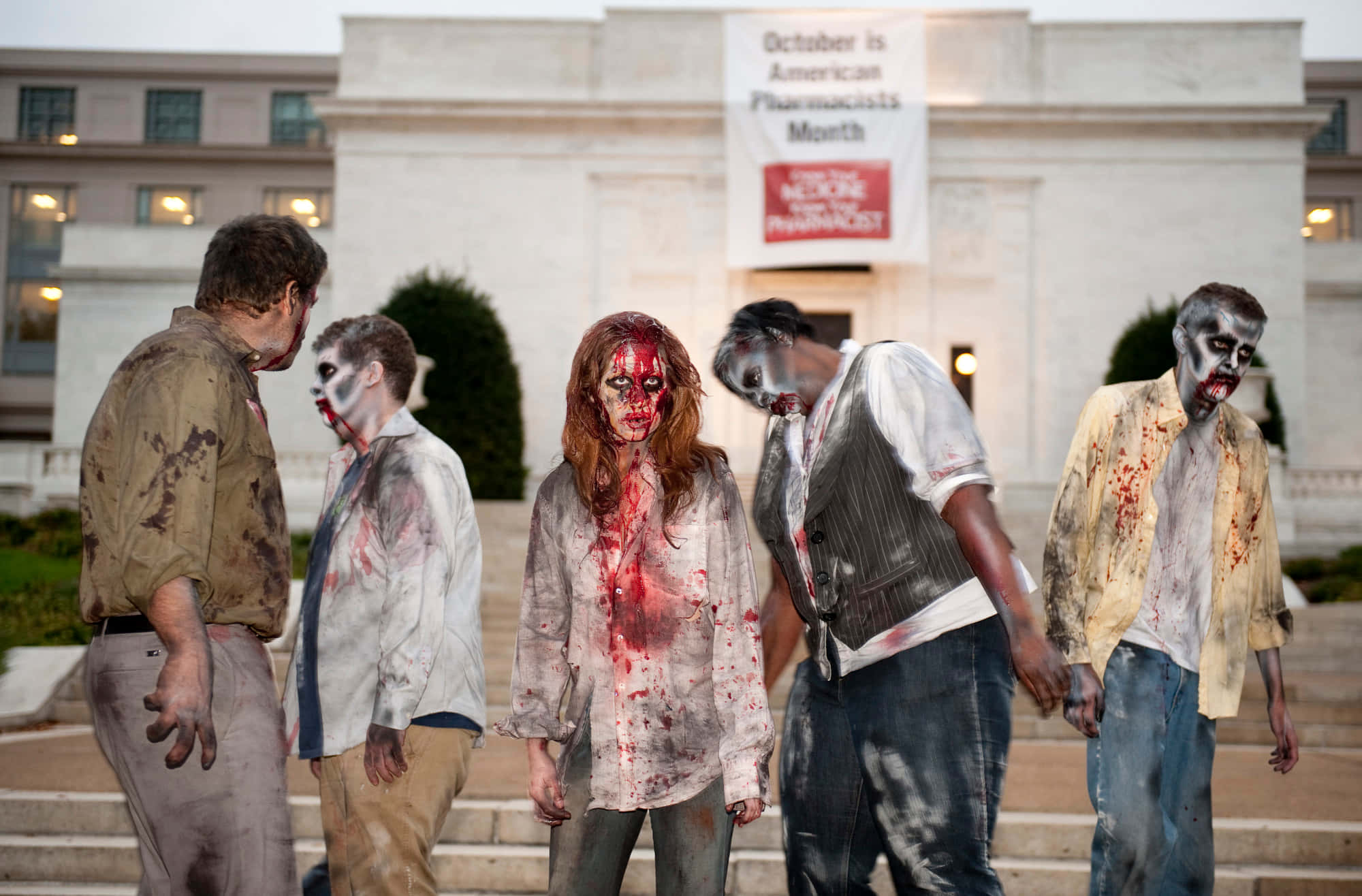 Undead 桌布 壁紙 — 五個化妝成殭屍、衣服沾滿血跡的人站在一棟掛有藥劑師月橫幅的建築物前的台階上。