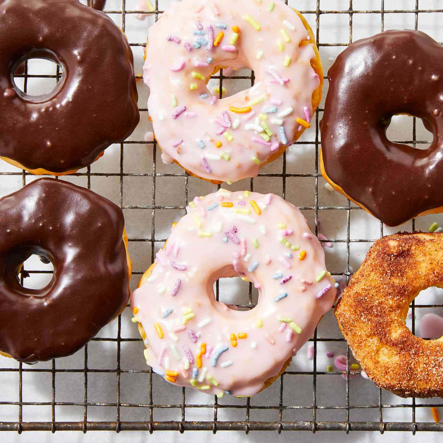 Glazed Donut 桌布 壁紙 — 五個塗有巧克力和粉紅色糖霜、頂部撒上彩色糖粒的釉麵甜甜圈放在金屬冷卻架上。