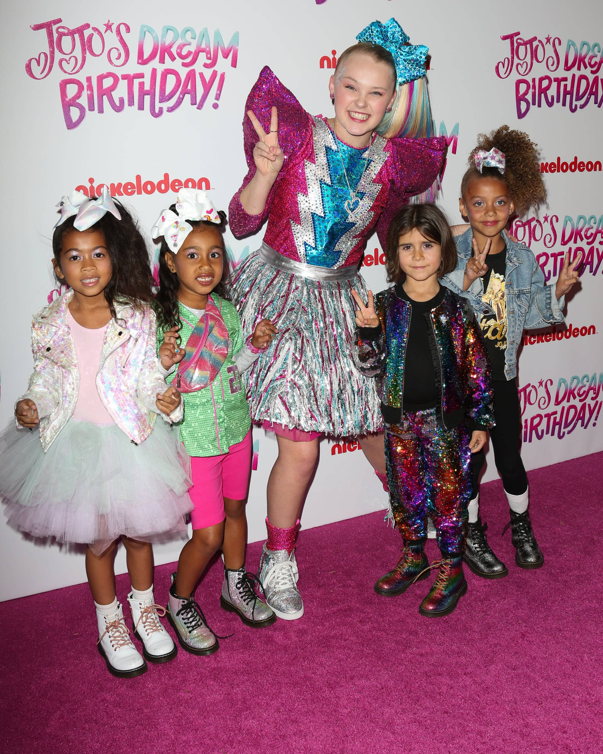 JoJo Siwa 桌布 壁紙 — 五個孩子穿著閃亮多彩的服裝，在Nickelodeon活動的粉紅色地毯上愉快地擺姿勢。