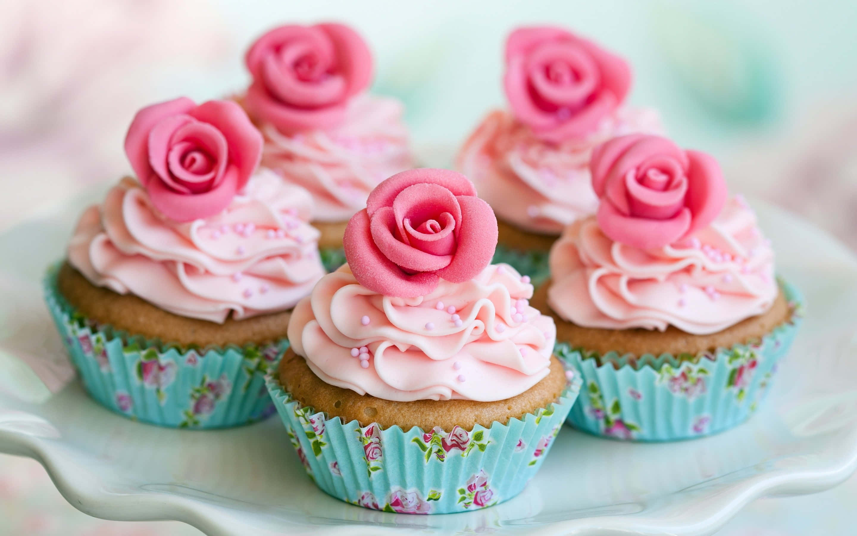 Cute Cupcake 桌布 壁紙 — 五個帶有粉紅玫瑰糖霜和花卉襯紙的杯子蛋糕，放在白色盤子上，背景是柔和的粉彩色。