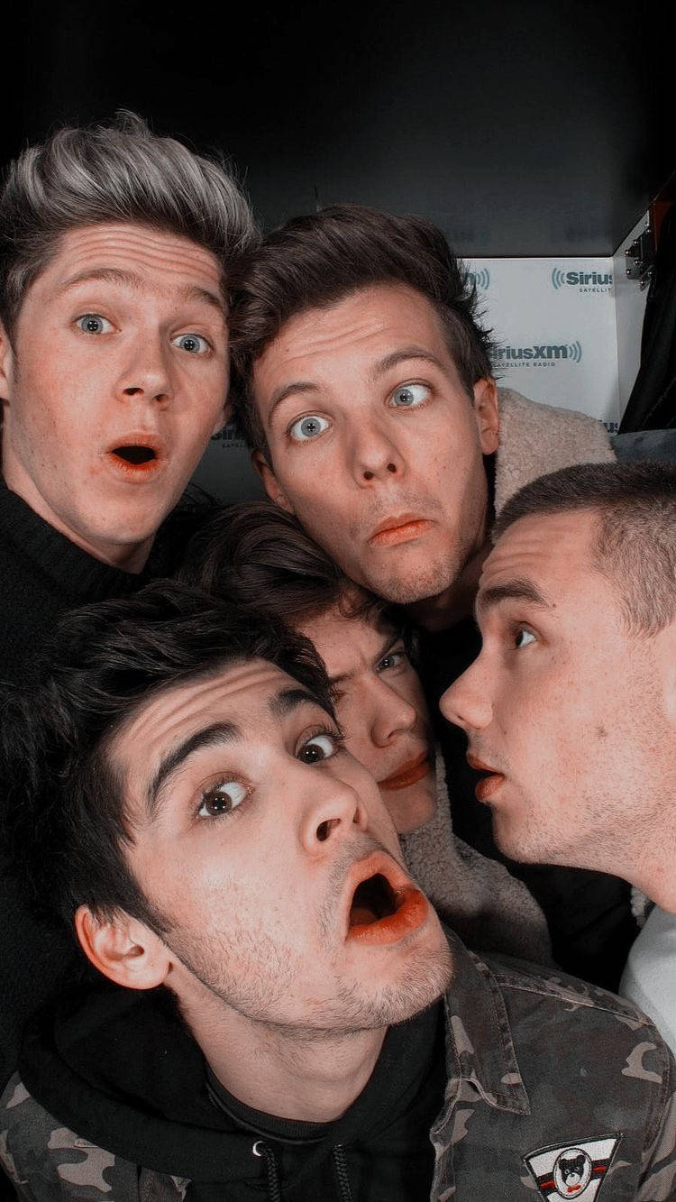One Direction Aesthetic 桌布 壁紙 — 五個年輕男子睜大眼睛，露出震驚的表情，在昏暗的室內環境中緊密地擠在一起。
