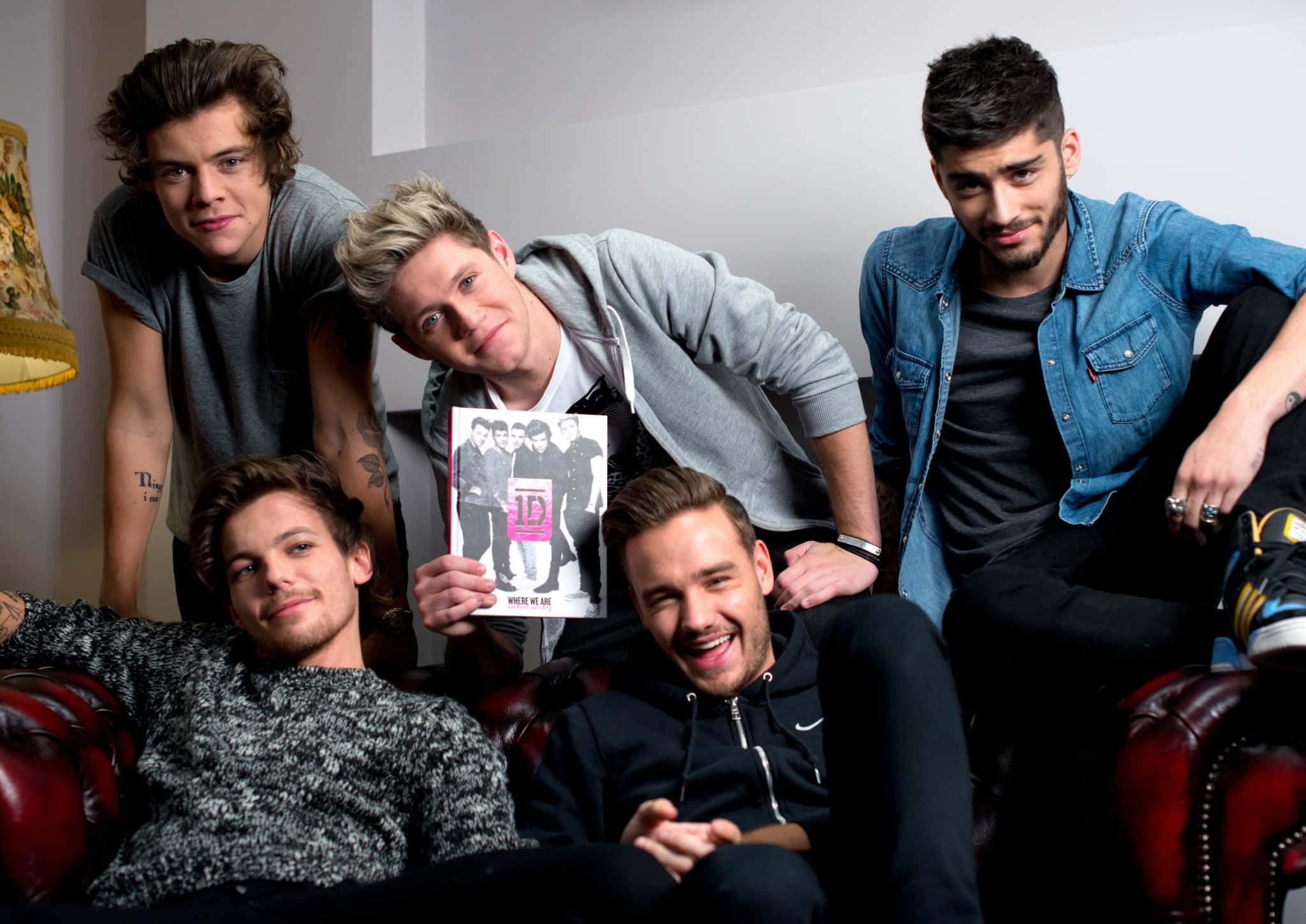 One Direction 桌布 壁紙 — 五個年輕男子隨意地一起坐在紅色皮沙發上，手持一張音樂專輯封面。