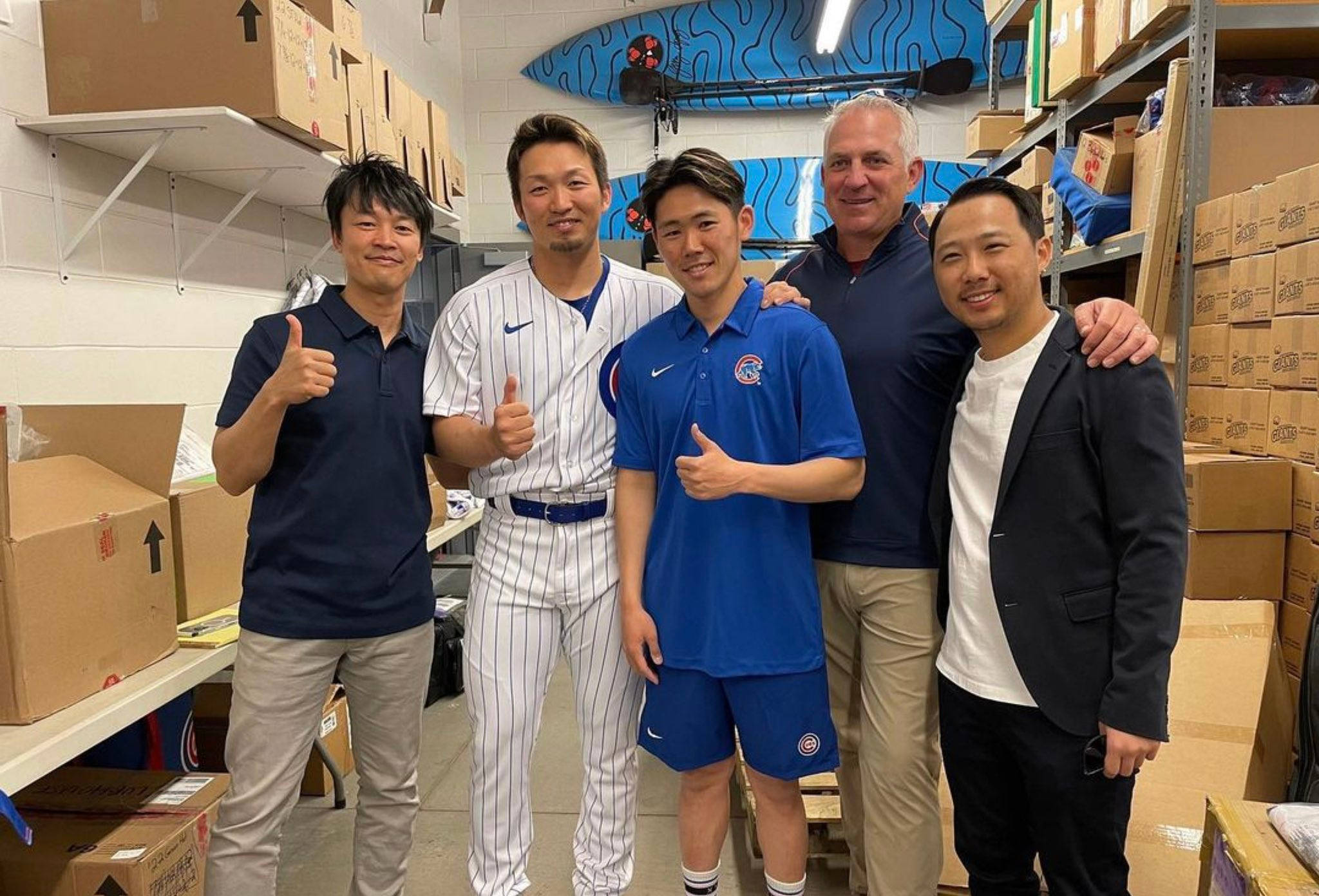 運動 桌布 壁紙 — 五個微笑的男人穿著棒球裝在一個裝滿紙箱和衝浪板的倉庫中一起擺姿勢。