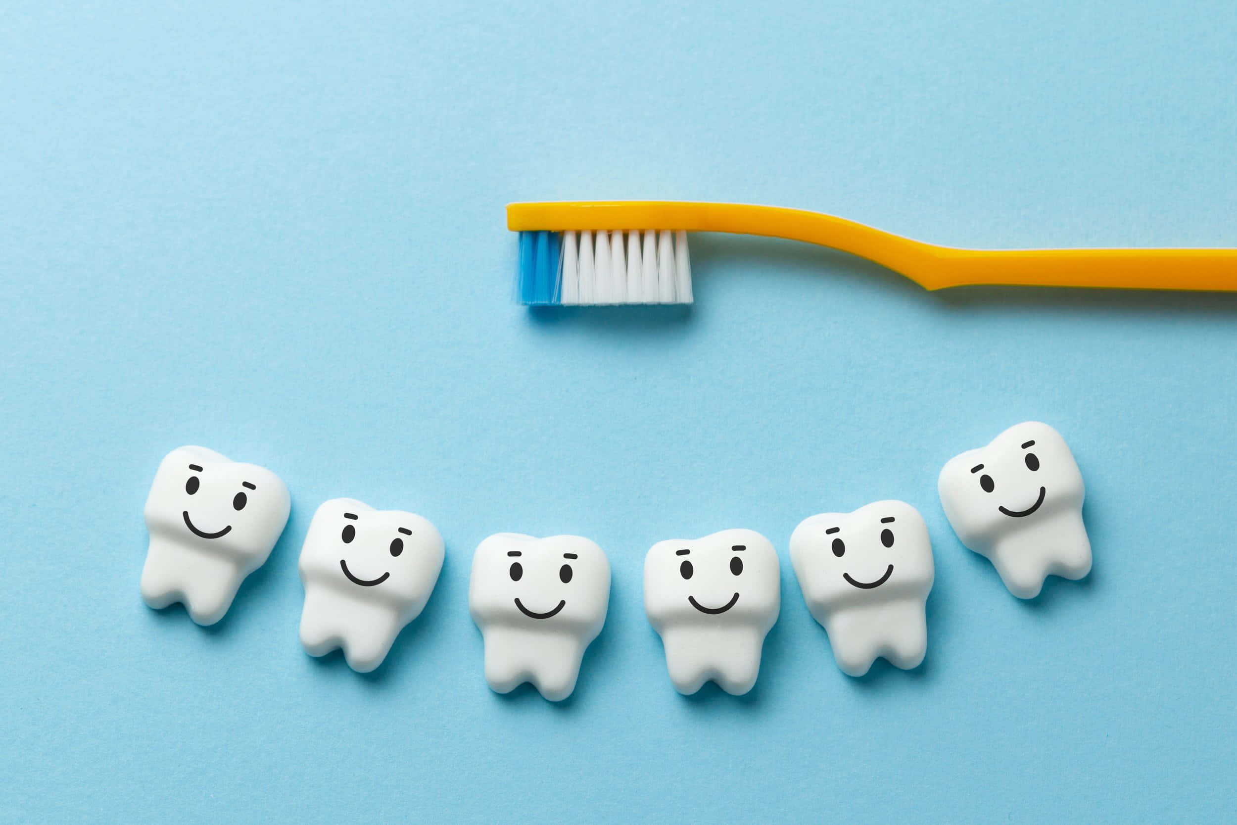 Tooth 桌布 壁紙 — 五個微笑的白色牙齒公仔排列在黃色牙刷下方，背景為純藍色。