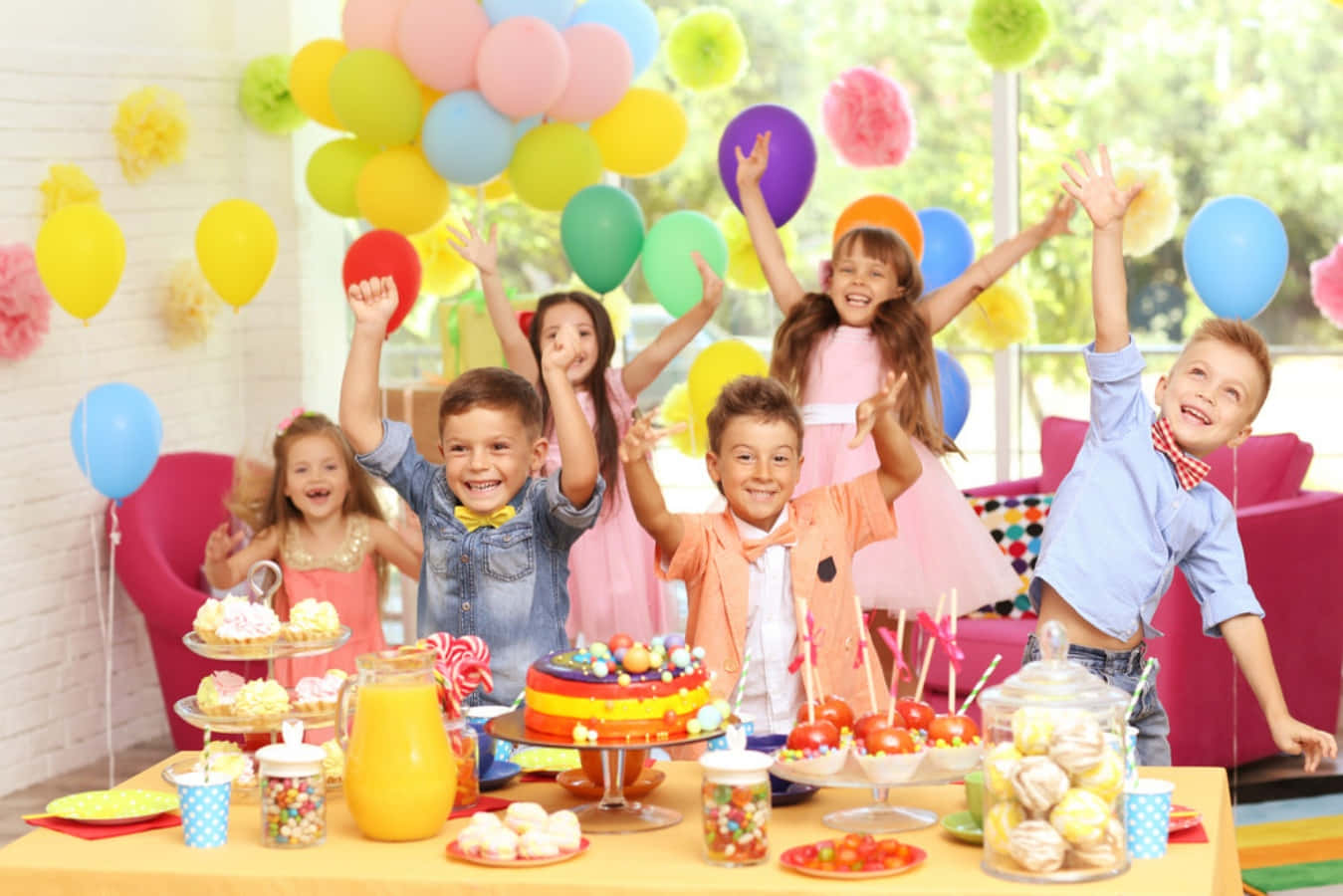 Birthday Celebration 桌布 壁紙 — 五個快樂的孩子在一個擺滿蛋糕、糖果和氣球的彩色生日桌旁舉起手臂慶祝。