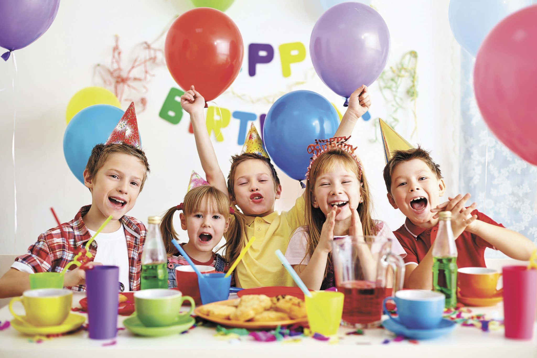 Birthday Party 桌布 壁紙 — 五個快樂的孩子戴著派對帽，在色彩繽紛的氣球和零食包圍下歡樂地慶祝生日。