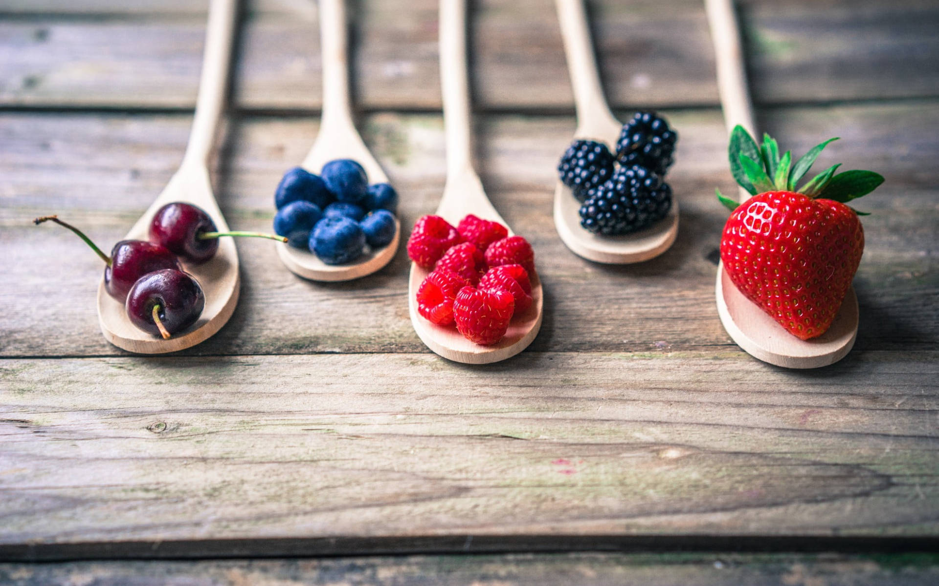 Berry 桌布 壁紙 — 五個木勺，每個盛放不同種類的新鮮漿果，整齊地排列在質樸的木質表面上。