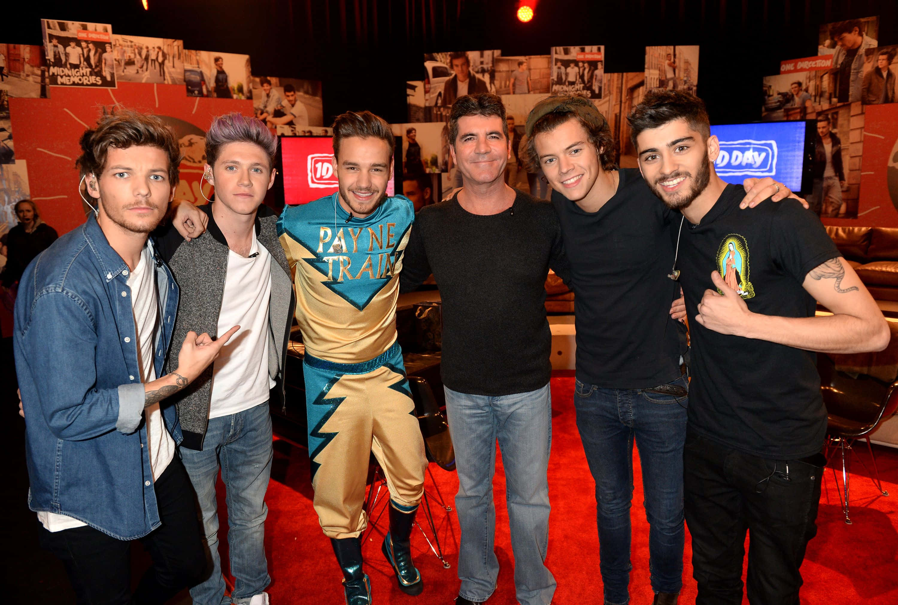 One Direction 桌布 壁紙 — 五個男人一起在紅地毯上擺姿勢，其中一人穿著色彩繽紛的Payne Train服裝，周圍環繞著照片和電視螢幕。
