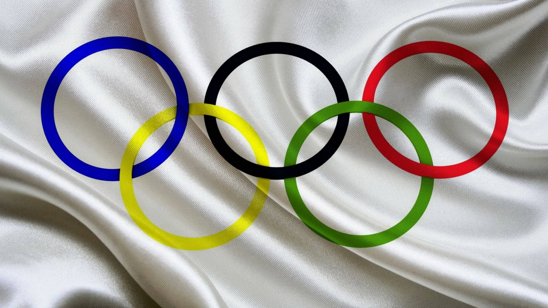 Olympics 桌布 壁紙 — 五個相互扣連的奧運環，顏色為藍、黃、黑、綠、紅，放置在帶有柔和皺褶的白色緞布上。