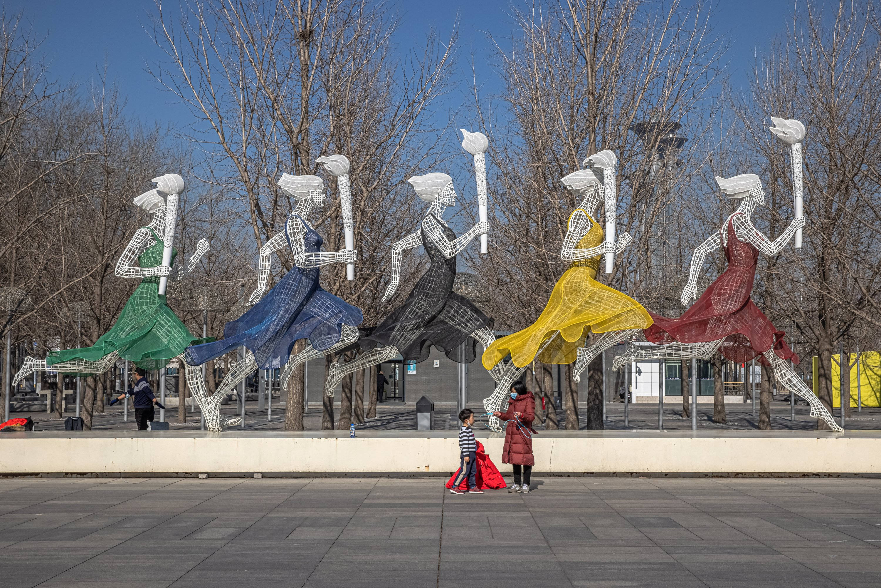 Winter Olympics 桌布 壁紙 — 五個穿著彩色連衣裙的線框跑者在晴朗藍天和光禿樹木下的廣場上衝刺。