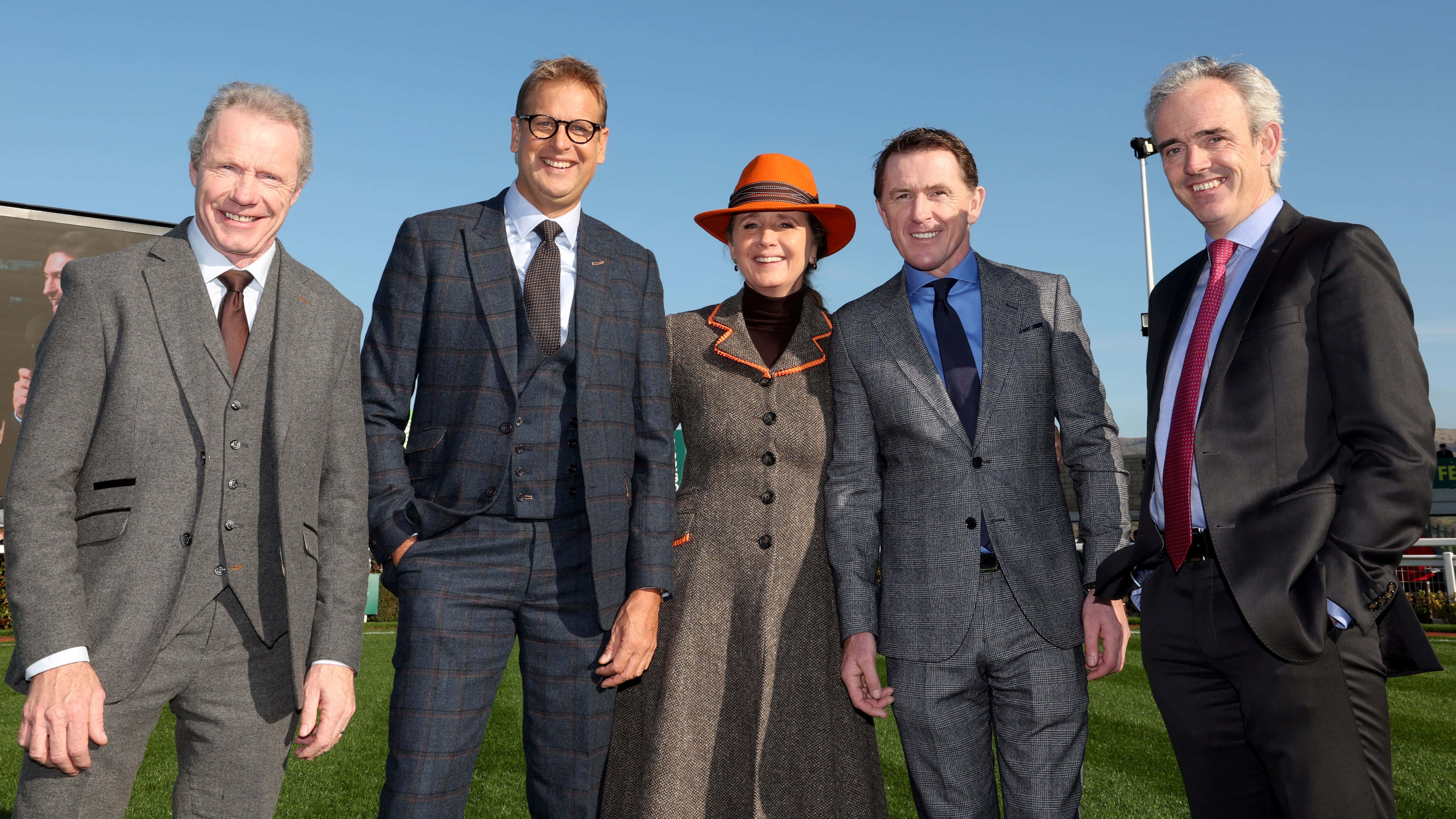 Cheltenham Festival 桌布 壁紙 — 五個穿著正式的人在陽光明媚的日子裡，在戶外活動中，在綠草藍天下為照片微笑。