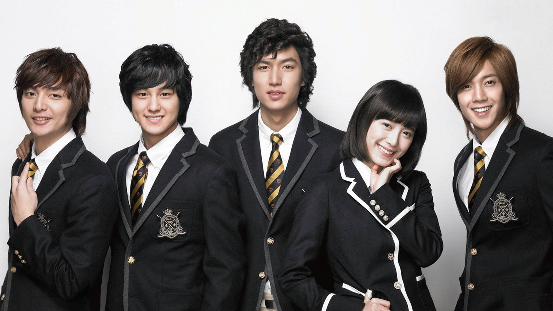 drama 桌布 壁紙 — 五個穿著黑色校服、帶有金色條紋和徽章的年輕人自信地在白色背景前擺姿勢。