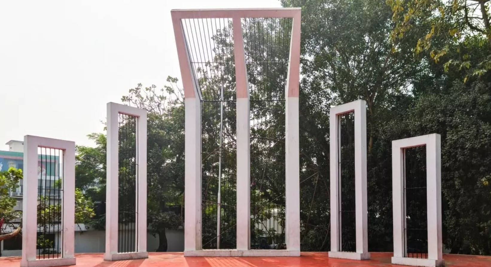 Dhaka 桌布 壁紙 — 五個粉紅色框的金屬閘門高度各異，矗立在紅色平台上，背景是晴朗天空下茂密的綠樹。